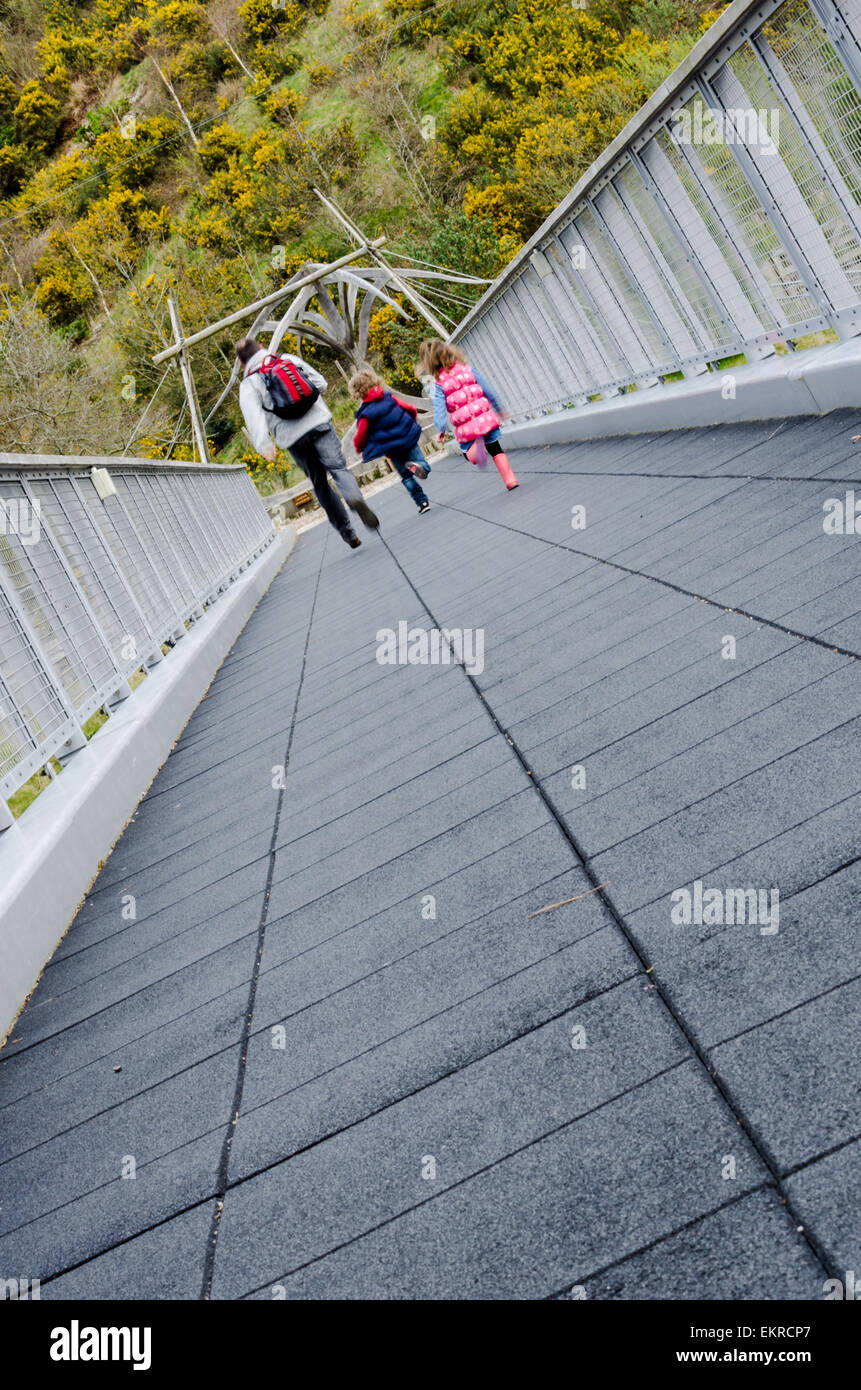 Dynamische Perspektive eines Vaters und seine kleinen Kinder zusammen, die entlang einer leeren Fussgängerbrücke. Stockfoto