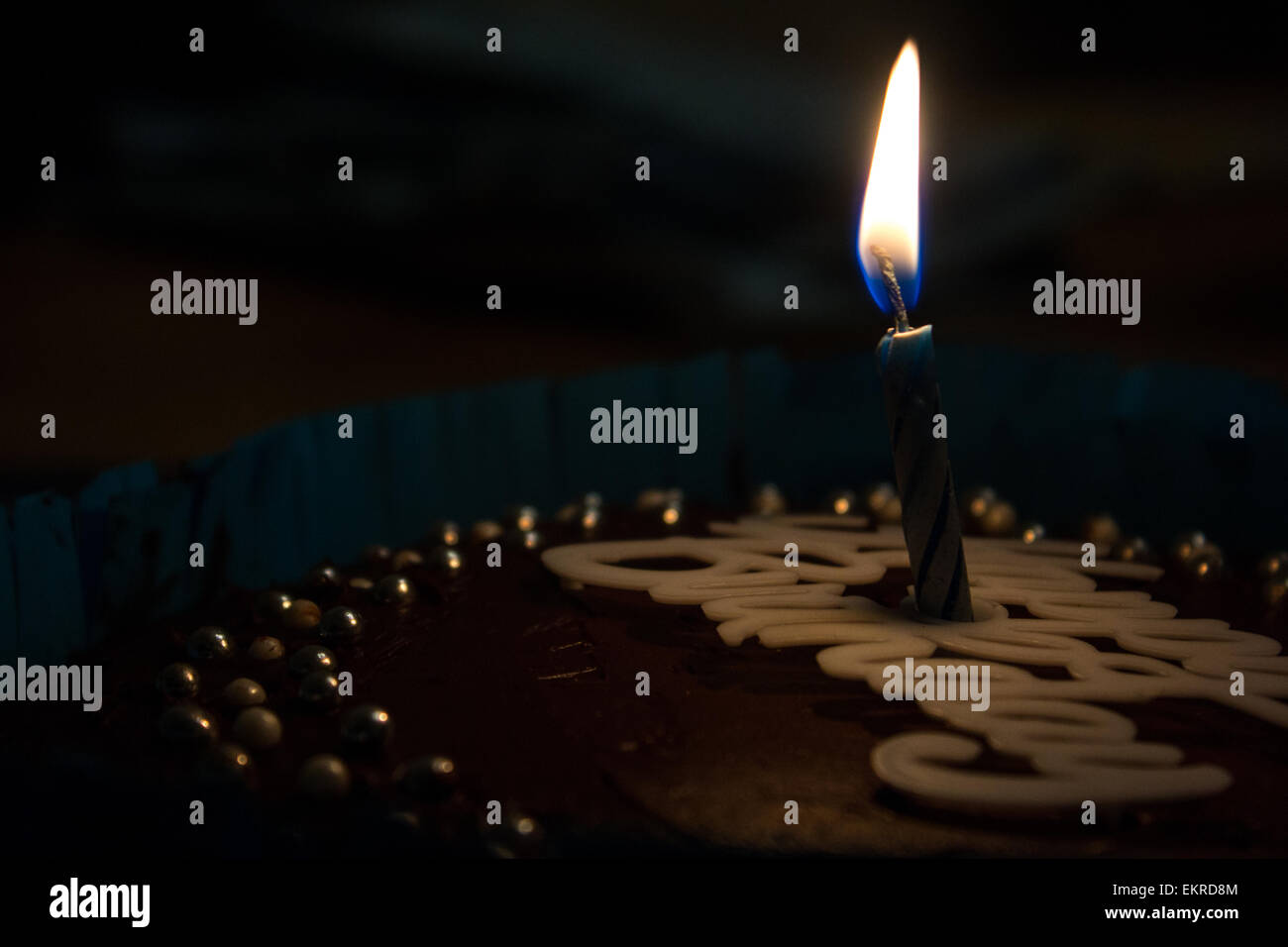 Blaue Kerze auf eine Schokolade Geburtstagskuchen in einem dunklen Raum. Stockfoto