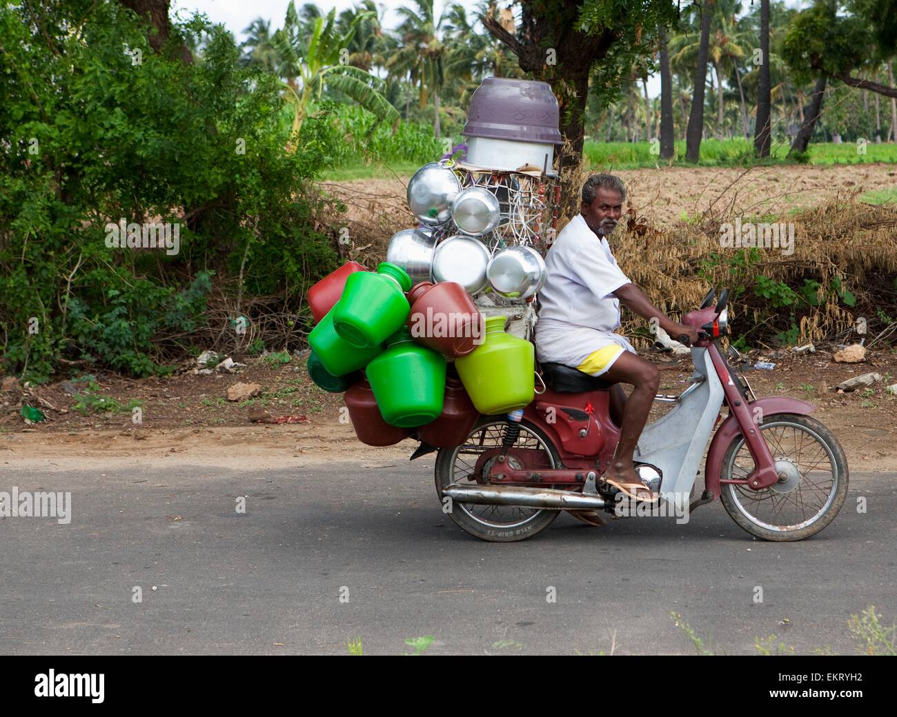 Ein Mann auf einem Motorrad mit vielen leeren Containern an es geschnallt, als er die Straße hinunter reitet; Sathyamangalam, Tamil Nadu, Indien Stockfoto