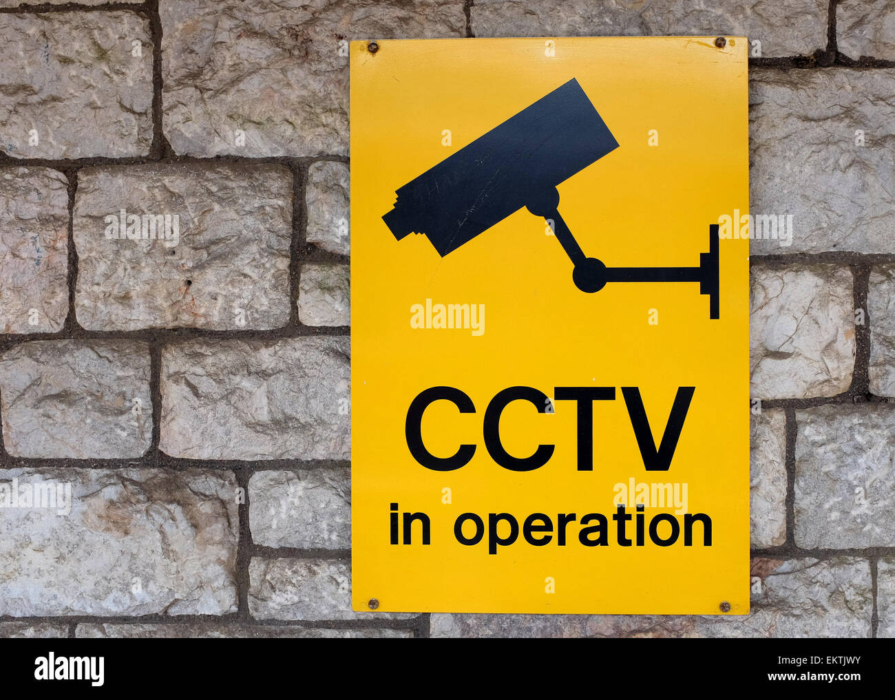 gelbes CCTV-Schild gegen eine Steinmauer Stockfoto