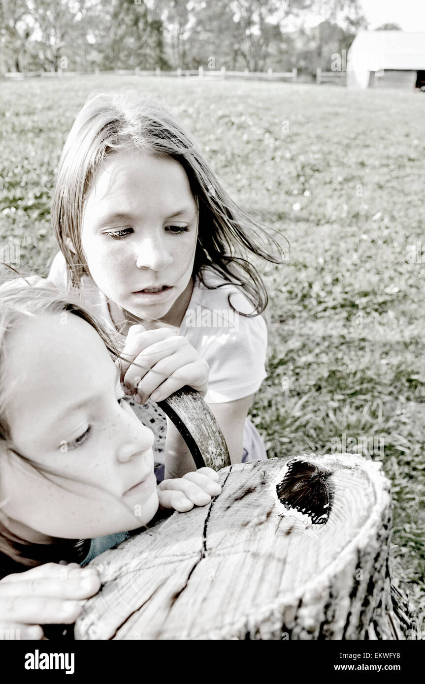 Zwei Mädchen beobachten einen Schmetterling auf einem hölzernen Pfosten Stockfoto