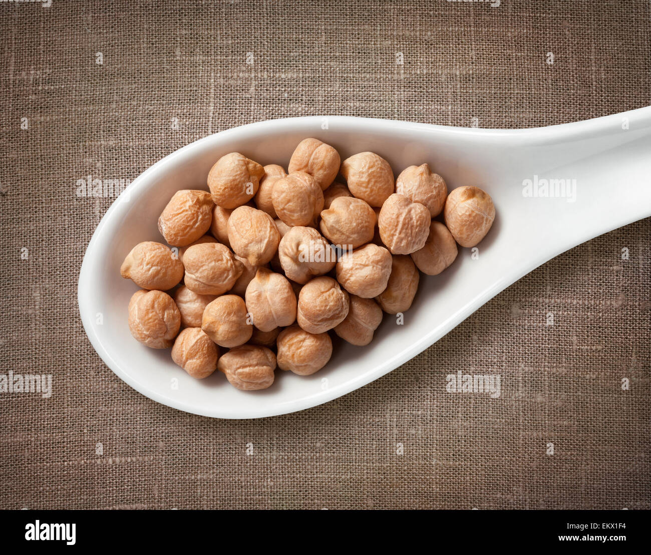 Kichererbsen in weißem Porzellanlöffel / Highres Foto von Korn in weißem Porzellan Löffel auf Jute Sackleinen Hintergrund Stockfoto