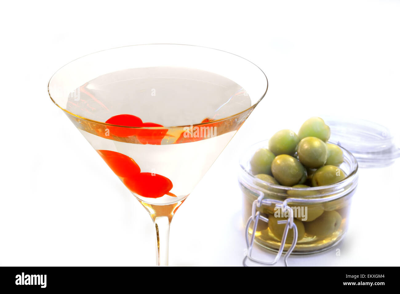 Ein Cocktailglas mit einer klaren alkoholisches Getränk und zwei Kirschen auf einen Stock, mit einem Container von Oliven im Hintergrund Stockfoto