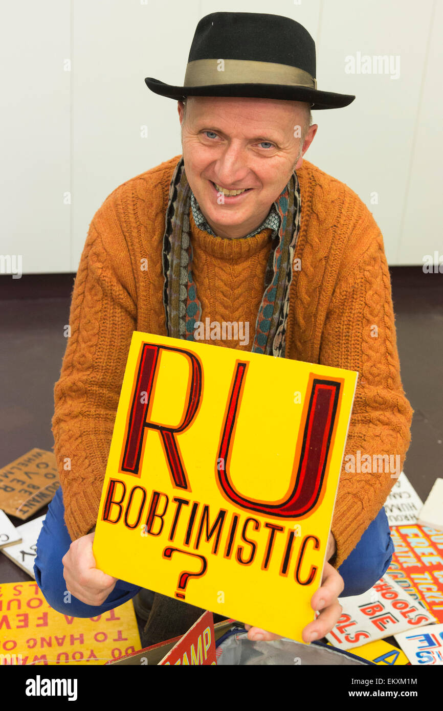 London, UK. 13. April 2015. Künstler Bob und Roberta Smith (orange Jumper) hält ein RU Bobtimistic Schild an der Cass, London Metropolitan University. Mehr als drei Wochen im Vorfeld der Parlamentswahlen als Künstler Bob und Roberta Smith (Patrick Brill) gegen Michael Gove im Surrey Heath Wahlkreis stehen wird Smith/Brill Studenten und Aktivisten The Arts Notrufzentrale in der Cass Bank Gallery in einem indoor Protest gegen Mittelkürzungen Kunst führen. Foto: Bettina Strenske Stockfoto