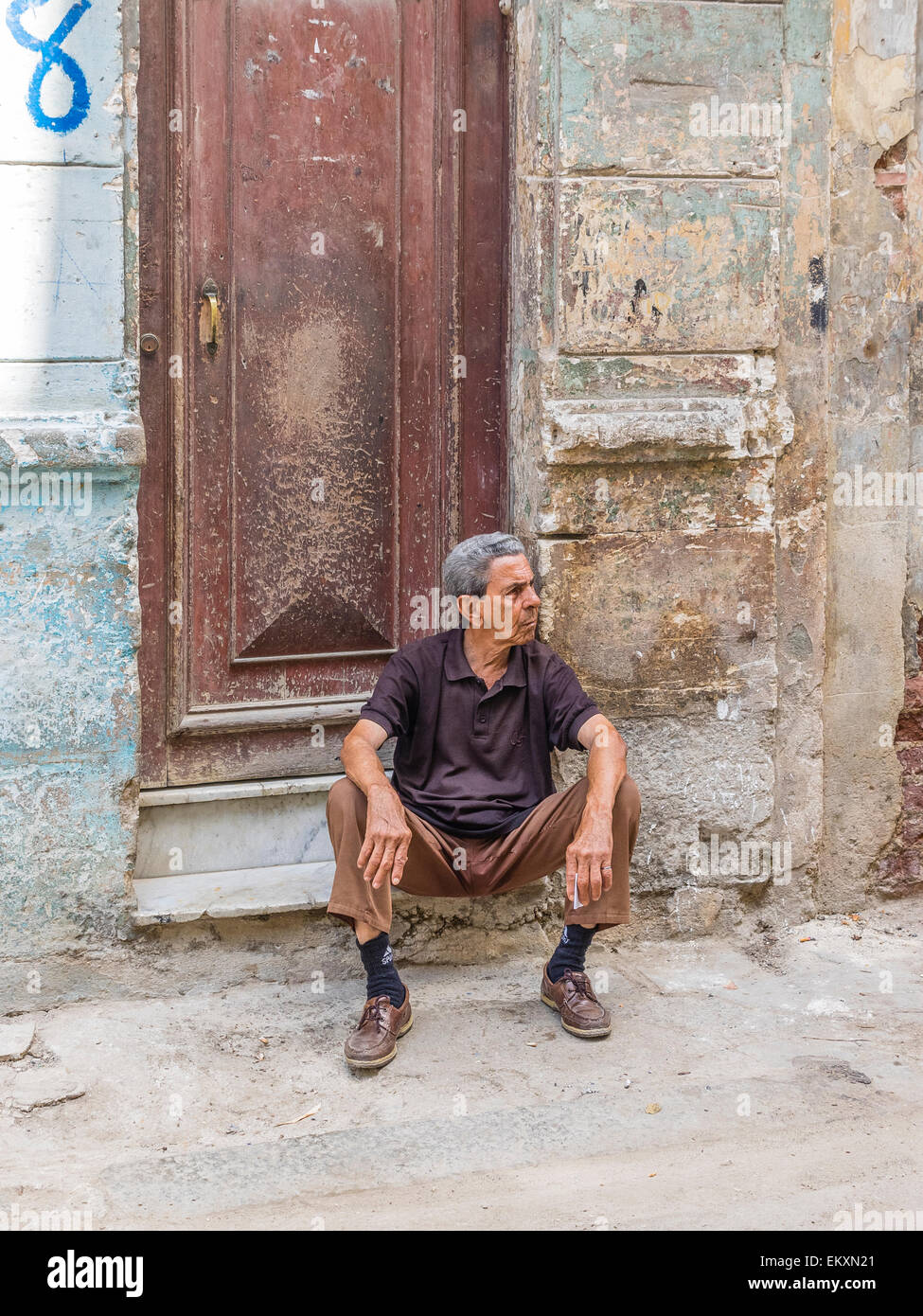 Ein kubanischen Hispanic Mann sitzt auf der Treppe vor seinem Haus mit bröckelnden Mauer in Havanna Vieja, Kuba. Stockfoto
