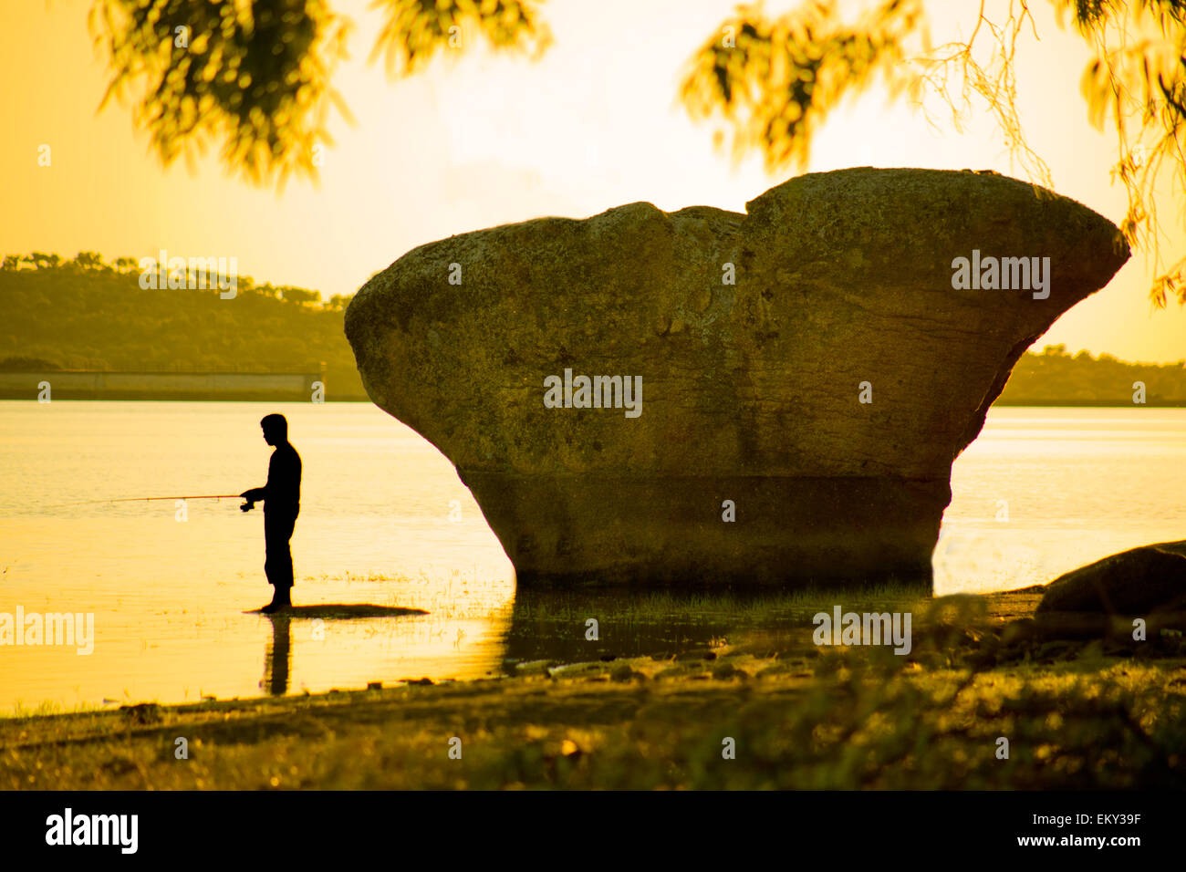 Ein Fischer stehen in der Nähe von großen Felsen in Damm bei Sonnenuntergang, Valdesalor, Caceres, Spanien Stockfoto