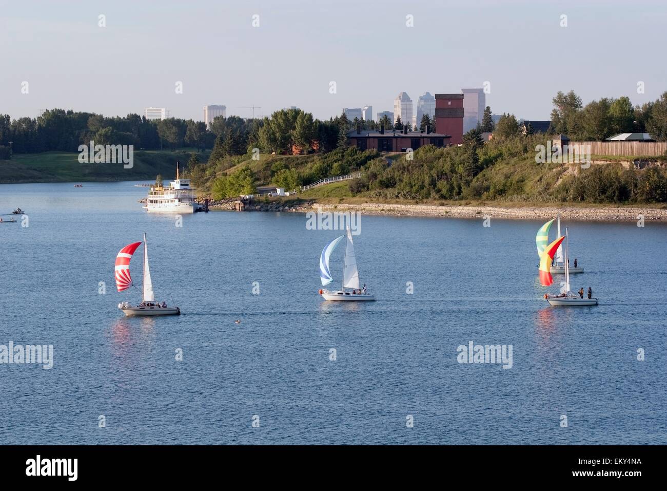 Calgary, Alberta, Kanada; Segelboote auf dem Wasser mit Heritage Park und die Stadt im Hintergrund Stockfoto