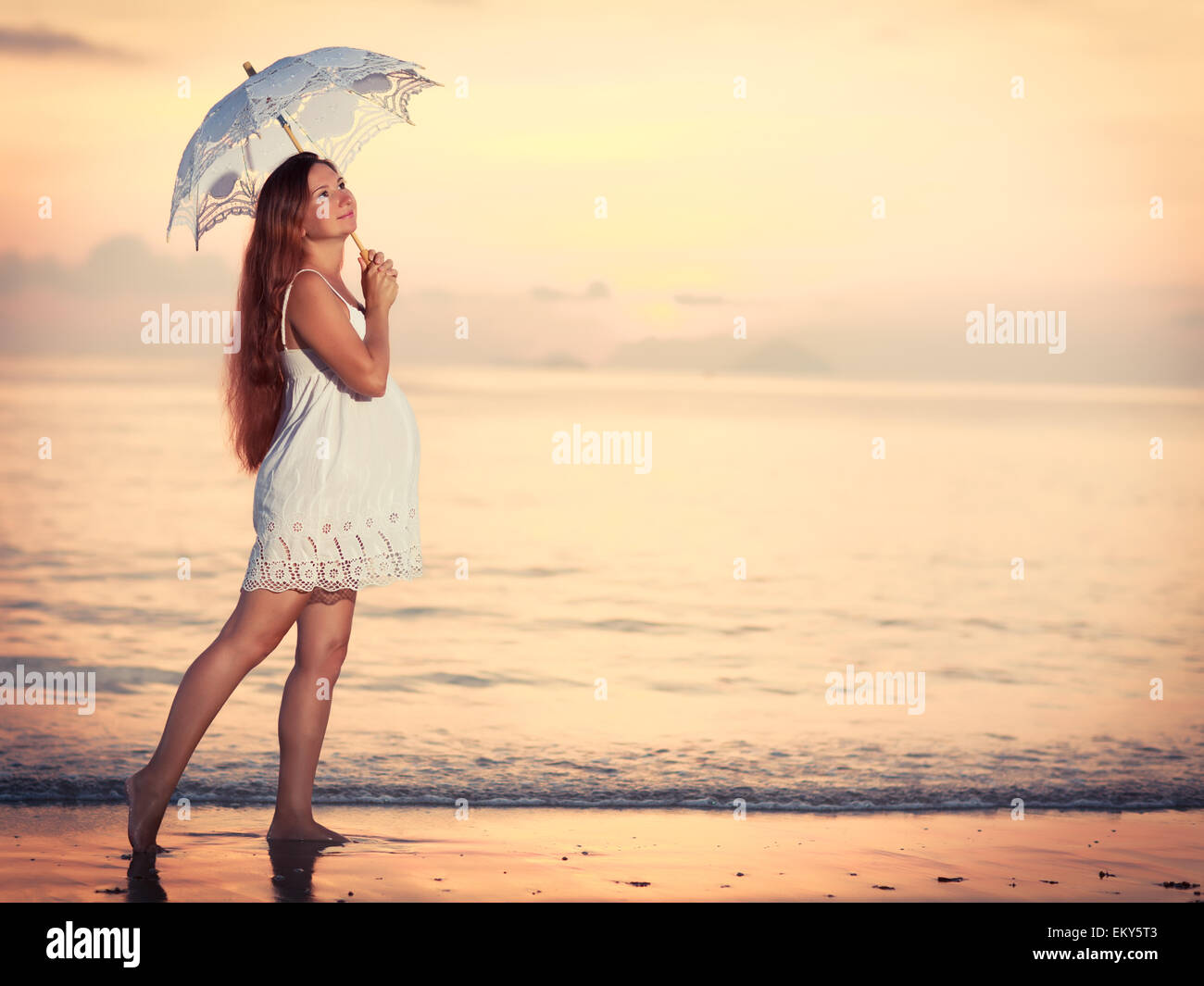 Schöne schwangere Frau bei Sonnenaufgang am Meer Stockfoto