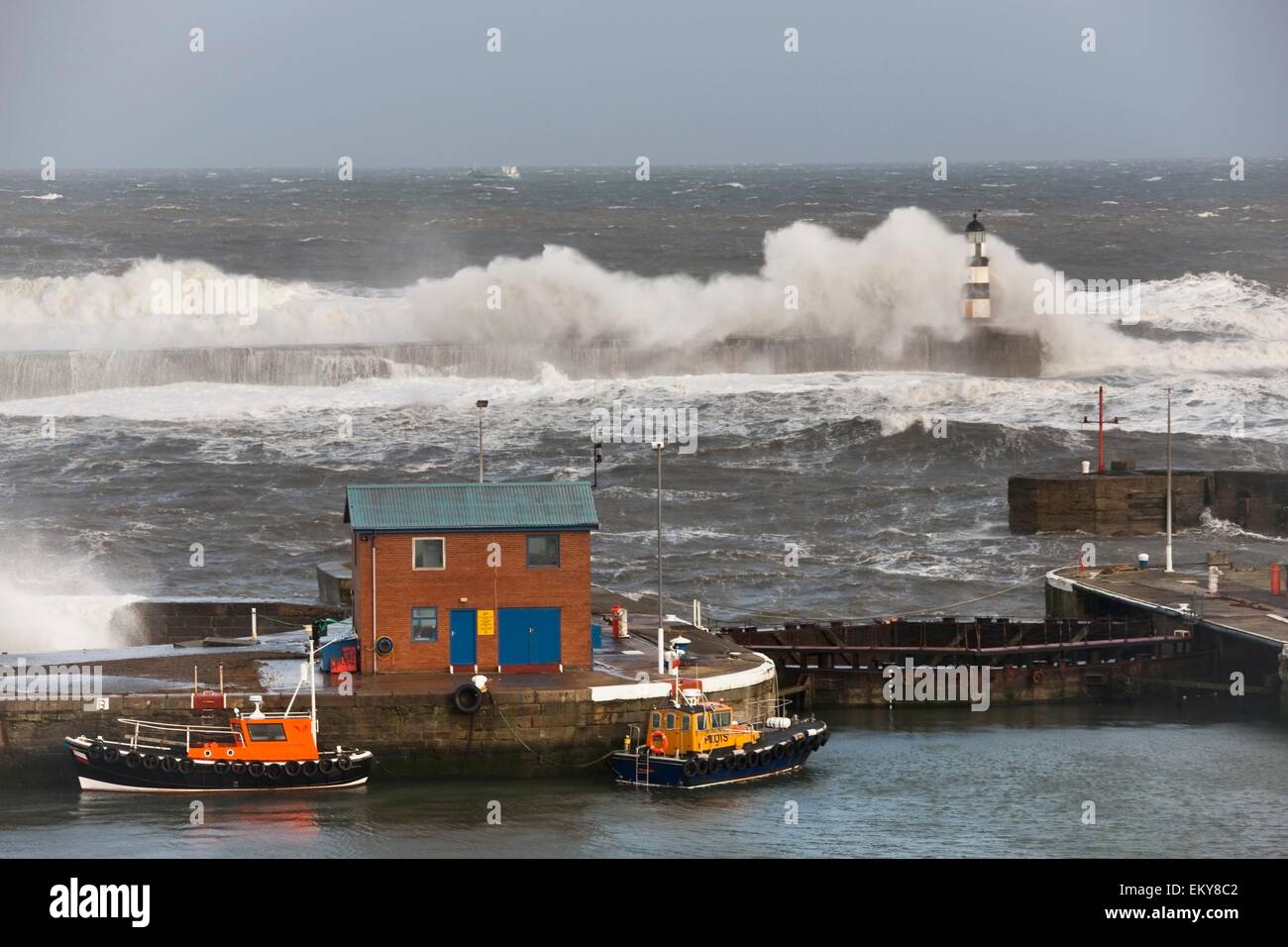 Seaham, Teesside, England; Wellen, die in einem Leuchtturm und Boote auf einem Pier Stockfoto