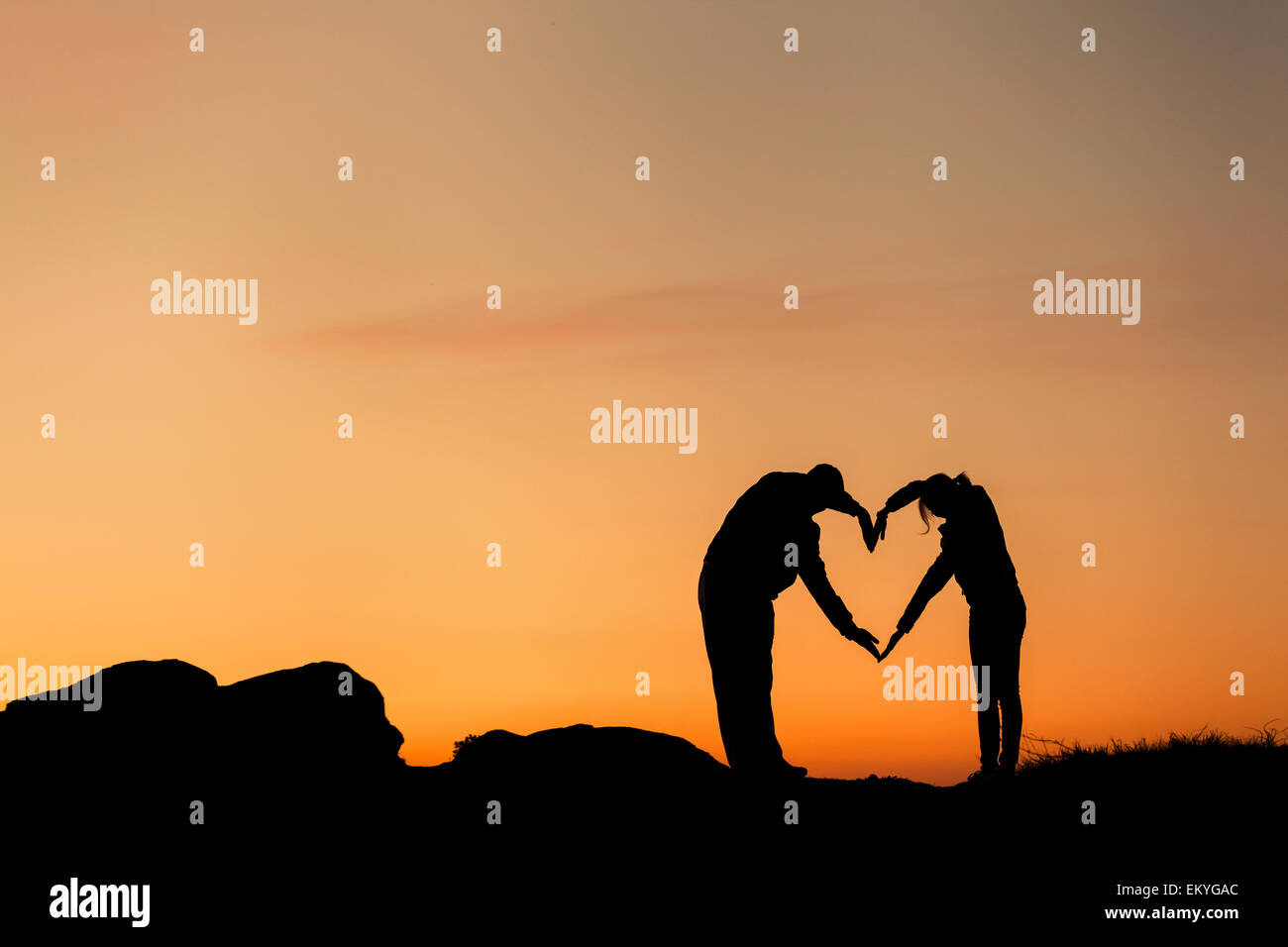 Konzeptionelle Herzform, Symbol des Menschen. Frau und Mann Hand Silhouette über Himmel bei Sonnenuntergang Hintergrund, Metapher, zu lieben Stockfoto
