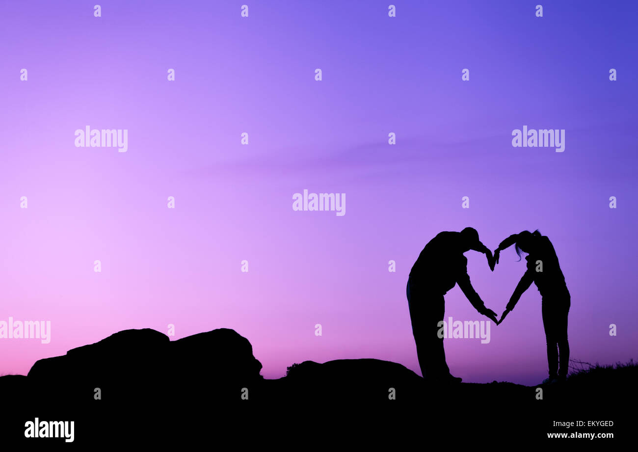 Konzeptionelle Herzform, Symbol des Menschen. Frau und Mann Hand Silhouette über Himmel bei Sonnenuntergang Hintergrund, Metapher, zu lieben Stockfoto