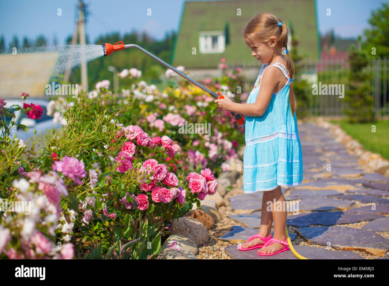 Süße Mädchen im blauen Kleid Blumen mit einem Schlauch in ihrem Garten gießen Stockfoto