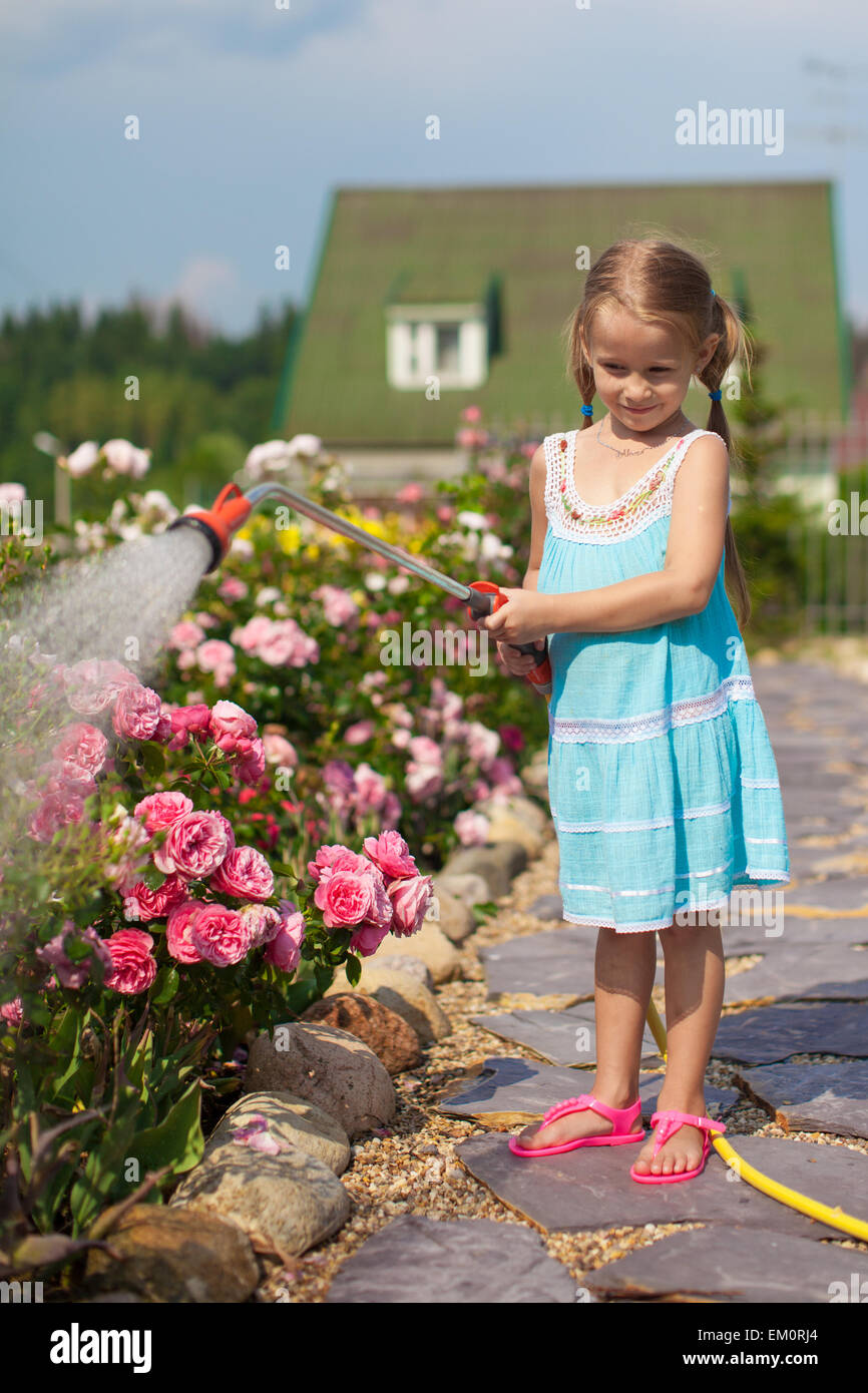 Kleines Mädchen im blauen Kleid Blumen mit einem Schlauch in ihrem Garten gießen Stockfoto