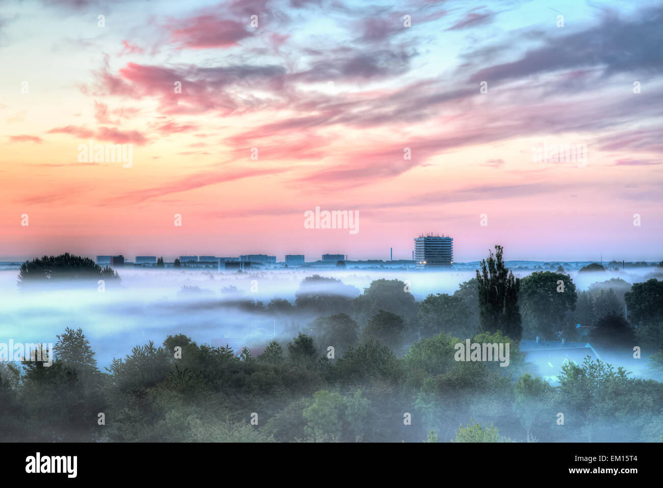 Eine hohe Bürogebäude über den Morgennebel. Die Sonne steigt erstellen Farben am Himmel. Stockfoto