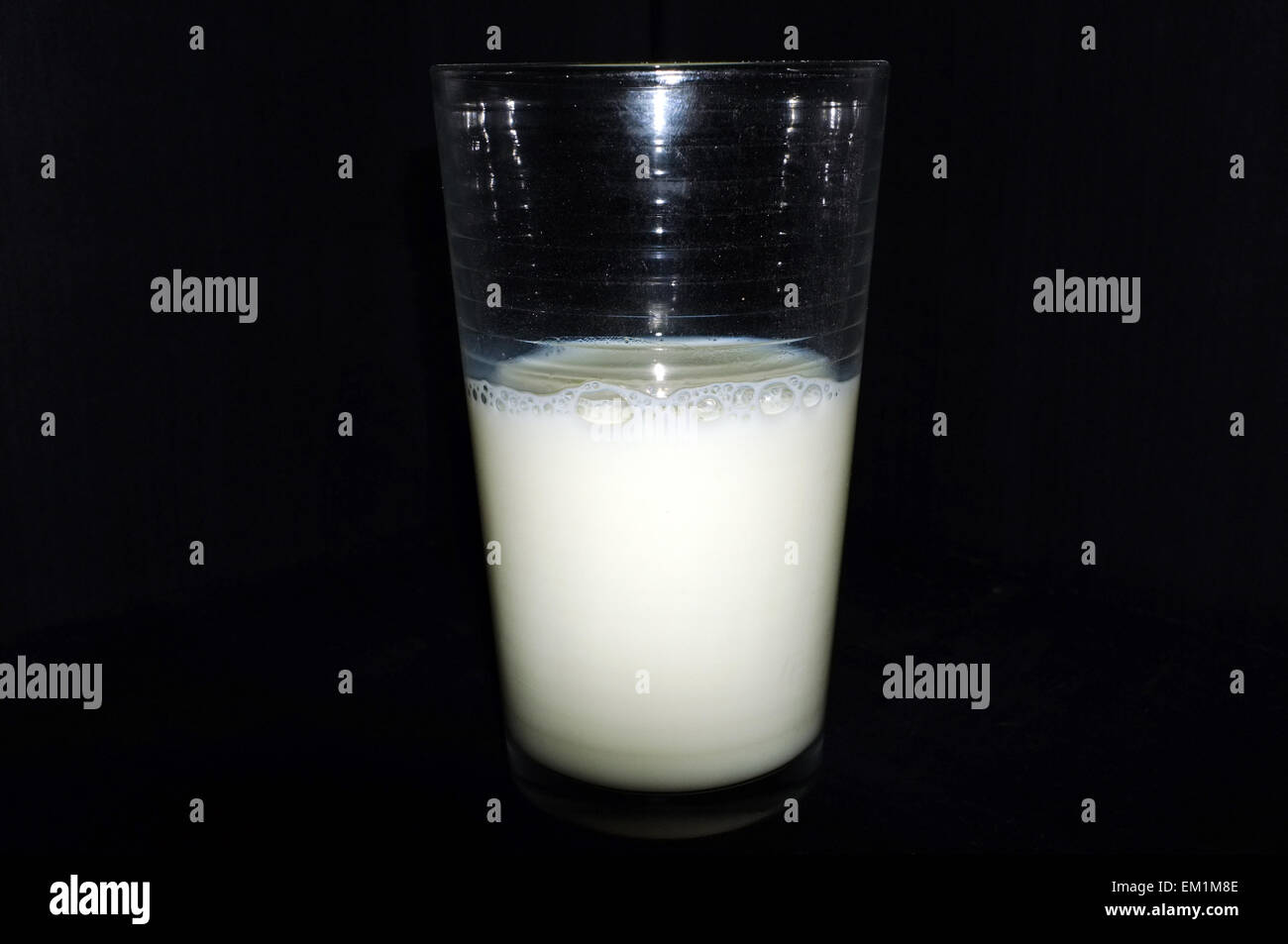 Ein Glas, das halb voll/halb leer Milch Muscheln vor einem schwarzen Hintergrund. Stockfoto