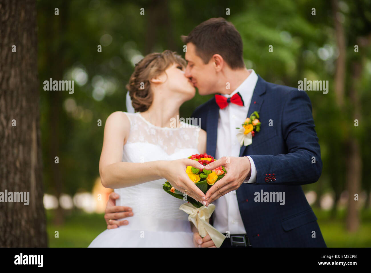 Glückliche Braut, Bräutigam, stehend im grünen Park, Hände zeigen Herz - Symbol der Liebe. Liebhaber in Hochzeitstag. glückliches junges Paar in der Liebe. Stockfoto