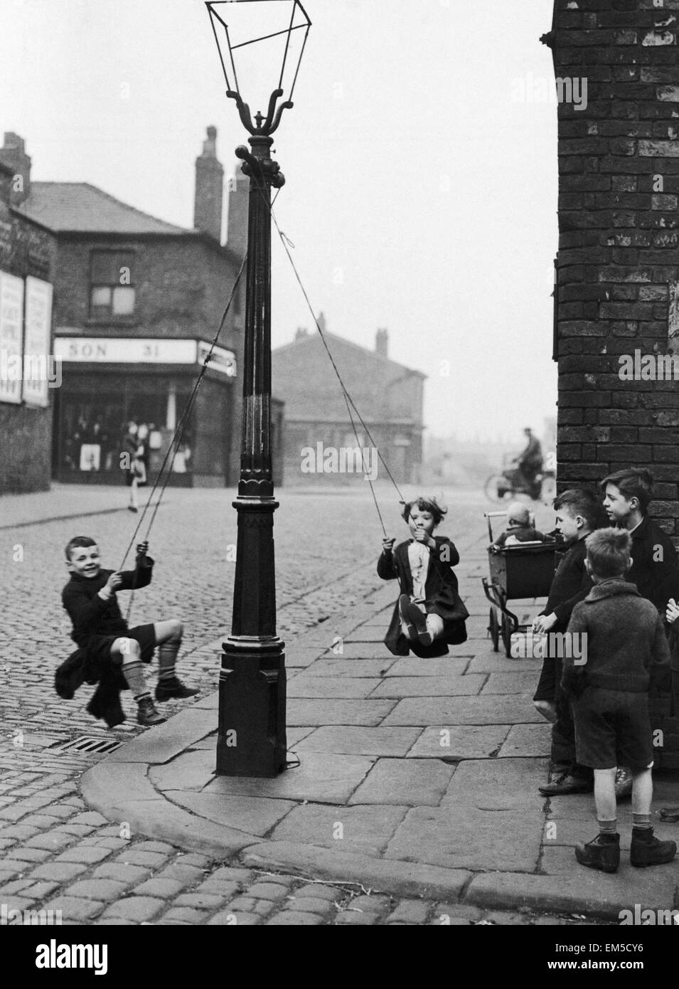 Kinder in einer Manchester Straße finden den eigenen Genuss mit Hilfe von einem Seil und einem Laternenpfahl. Kinder spielen auf der Straße, im März 1943 von einer Straßenlaterne schwingen. Stockfoto