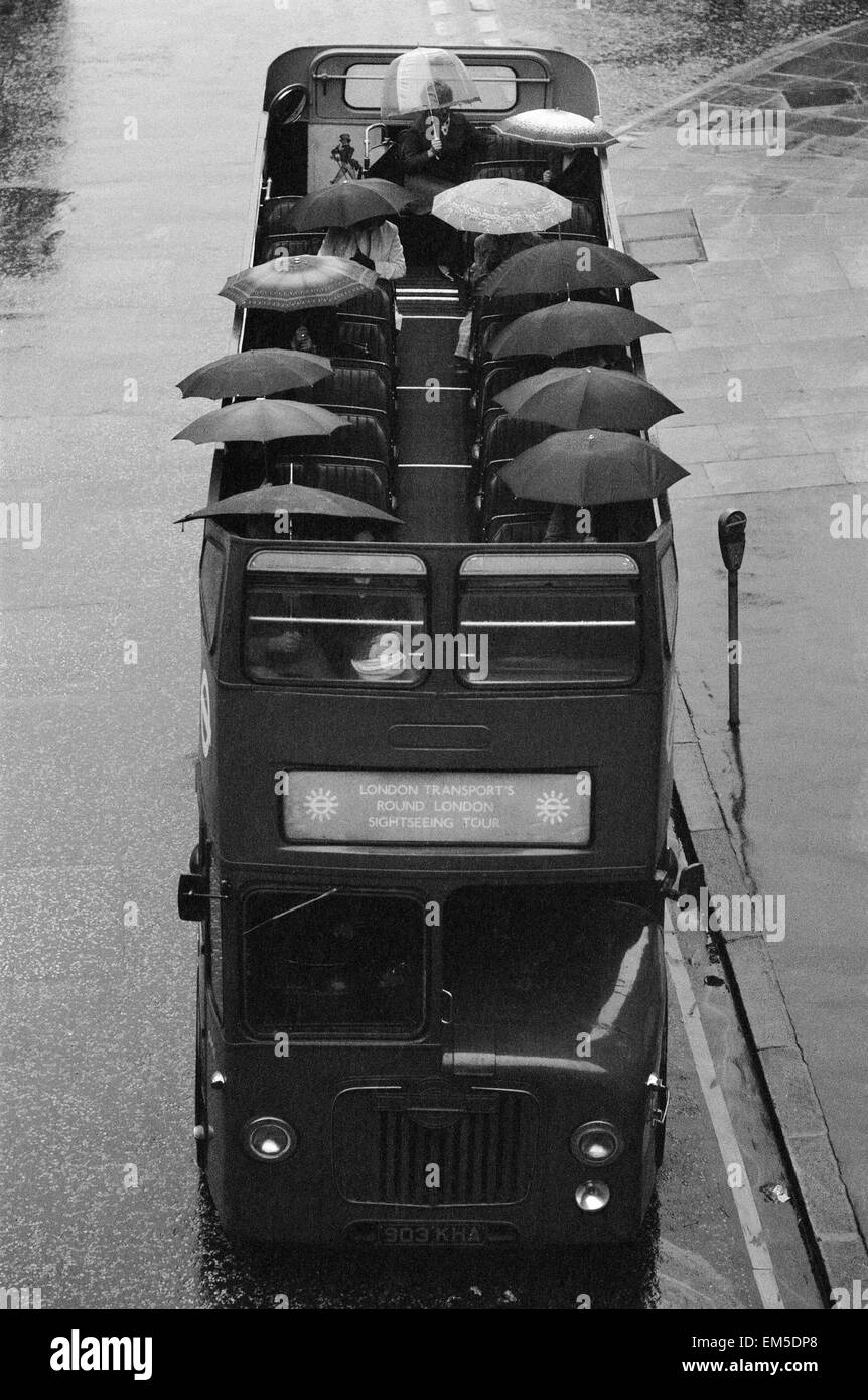Touristen sitzen unter ihren Regenschirmen auf dem oberen Deck von einem offenen Bus während einer Sightseeing-Tour durch London im Regen. 28. Oktober 1976. Stockfoto