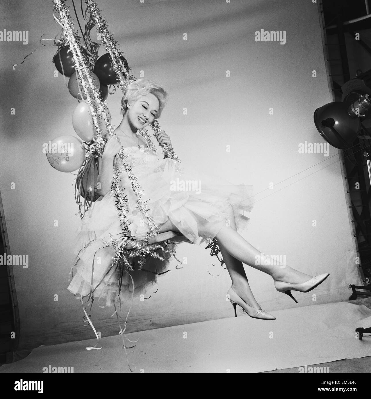 Schauspielerin Carole Leslie posiert im Studio trägt ein weißes Kleid, sitzt auf einer Schaukel mit Weihnachtsschmuck. 24. Dezember 1958. Stockfoto