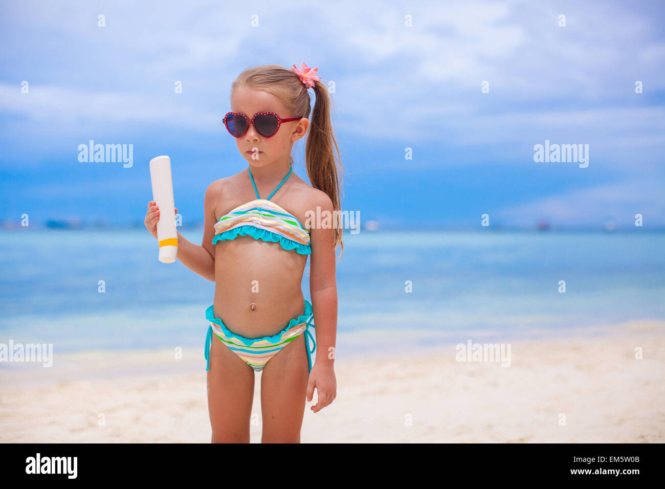 Entzückendes Mädchen im Badeanzug hält Suntan Lotion Flasche Stockfoto