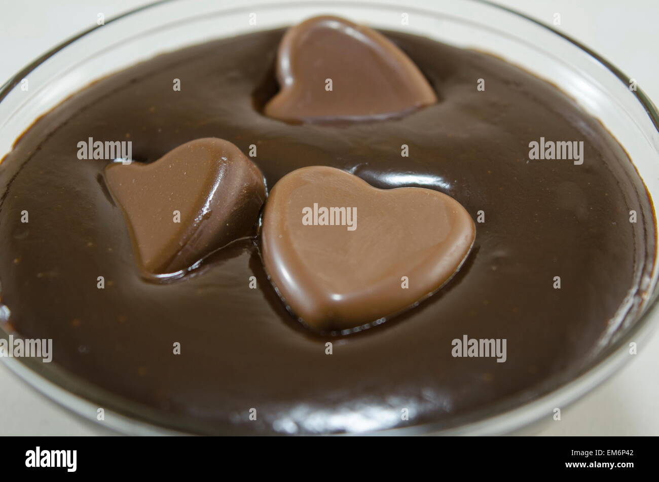 Schokoladenherzen schwimmen in einer tiefen Glasplatte mit geschmolzener Schokolade gefüllt Stockfoto