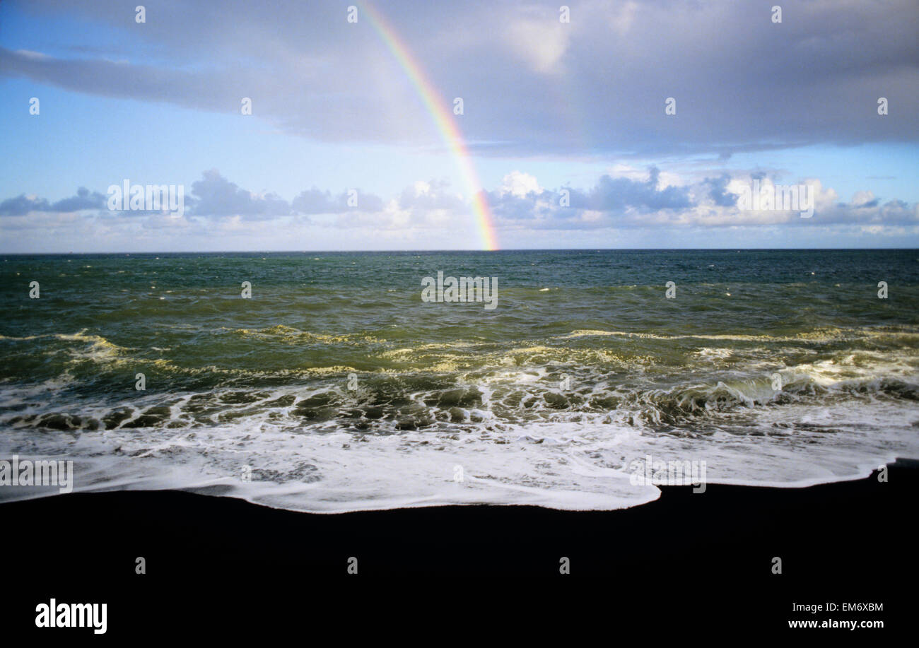 USA, Hawaii, Regenbogen über dem Pazifischen Ozean und schwarzen Sandstrand in Hawaiʻi-Volcanoes-Nationalpark; Big Island Stockfoto