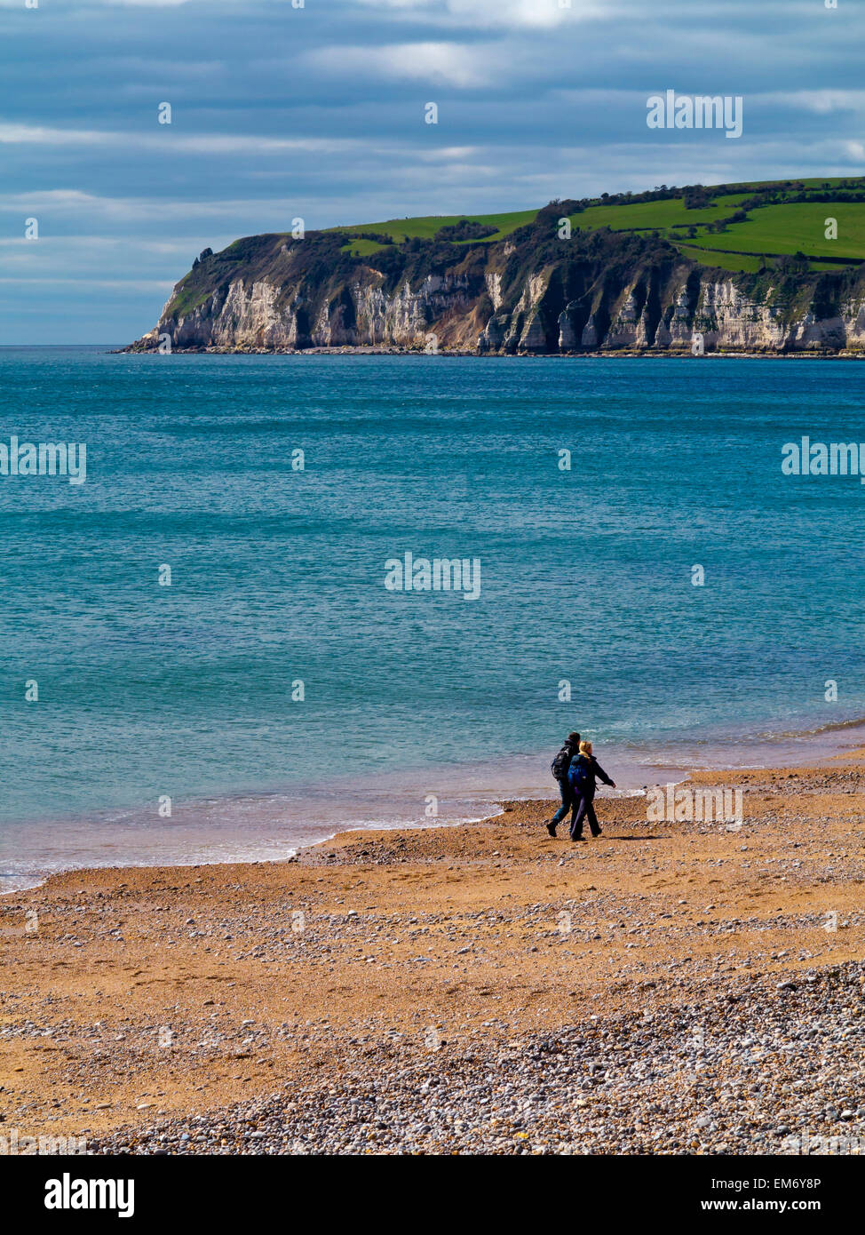 Foto eines Paares zu Fuß entlang am Strand von Seaton East Devon England UK und Blick nach Westen in Richtung Bier Stockfoto