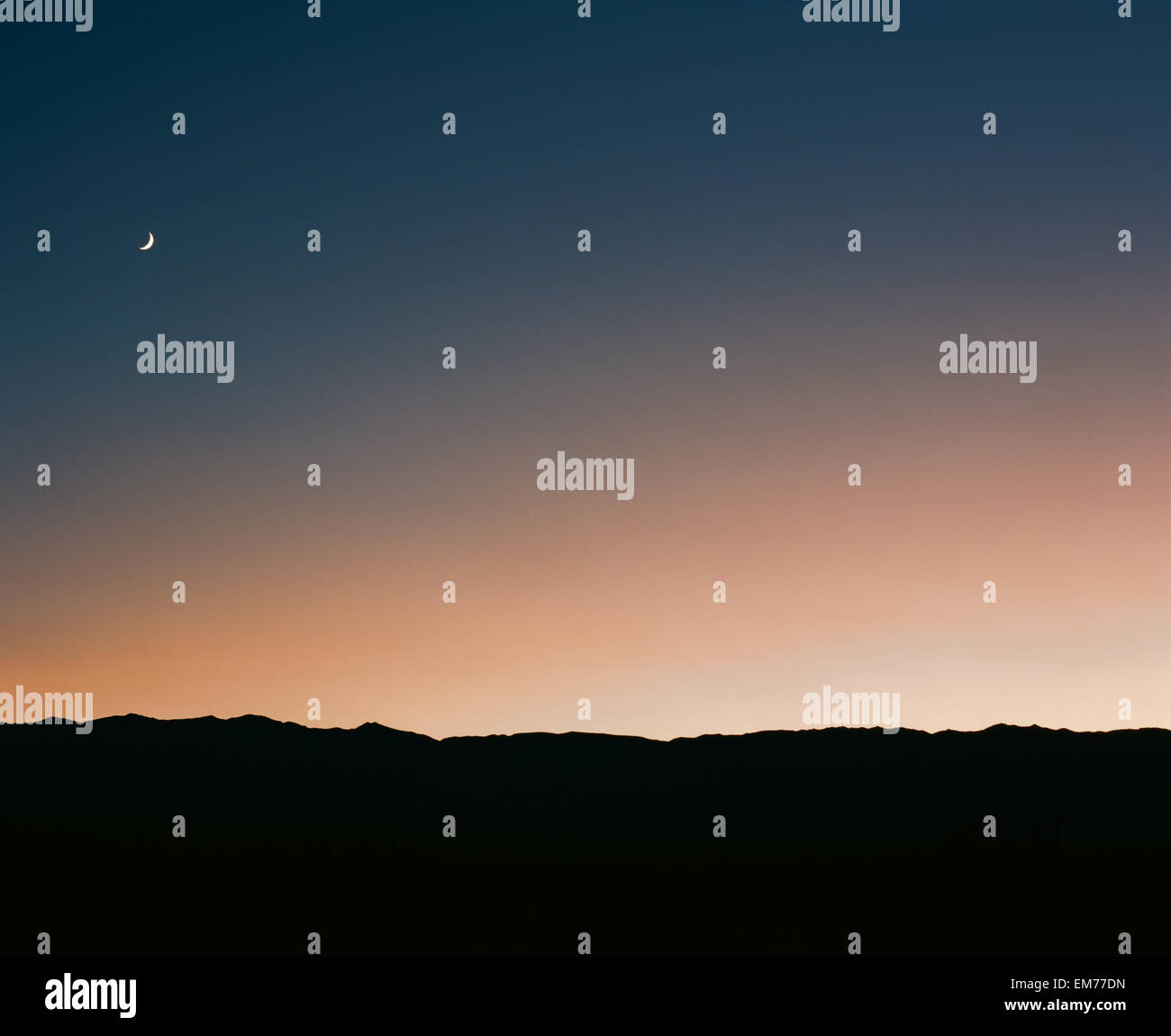Mondaufgang über die Silhouette einer Wüstenlandschaft direkt nach dem Sonnenuntergang gegen einen Farbverlauf von blau und orange sky Stockfoto