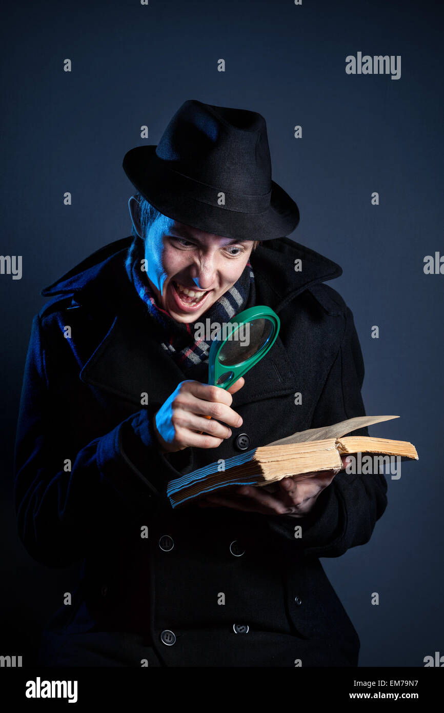Emotionale Mann in schwarzer Hut mit Lupe, die das alte Buch bei dunklem Hintergrund Stockfoto