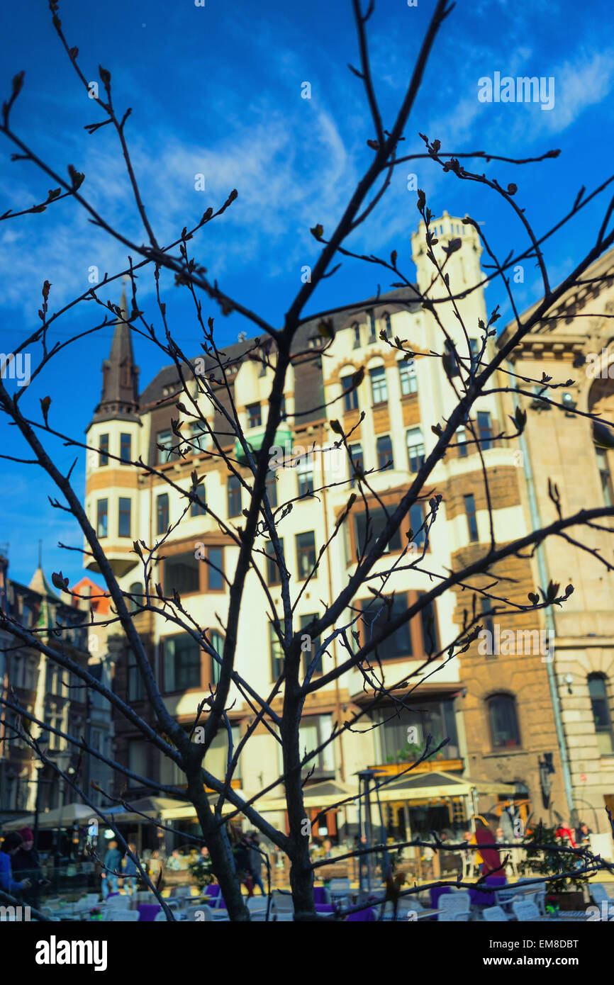 Alte Gebäude und Open-Air-Cafés über die Web-Äste ohne Blätter an einem hellen Frühlingstag in Riga Stockfoto