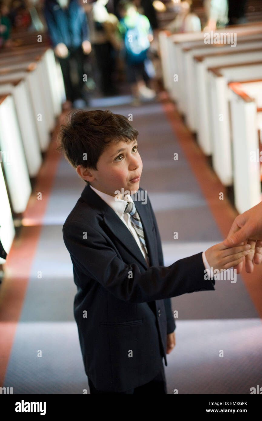 Sieben Jahre Alter spanischer Junge schüttelt die Hand des Priesters in der Kirche nach Erhalt der Sacrement der Erstkommunion.  Model-Release Stockfoto