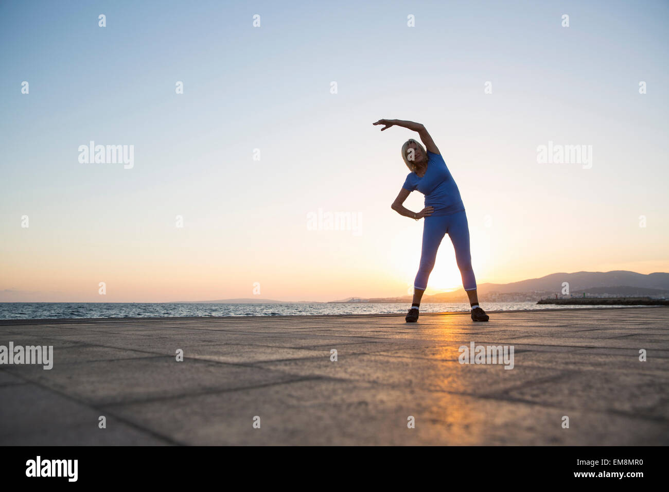 Ältere Frau erstreckt sich vom Strand Stockfoto