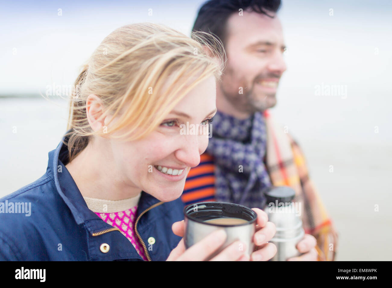 Paar am Strand, heißes Getränk aus Getränke Flasche trinken Stockfoto