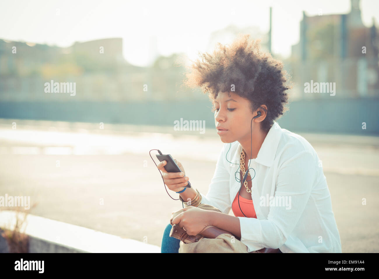 Junge Frau, die Auswahl der Musik auf Smartphone in Stadt Stockfoto