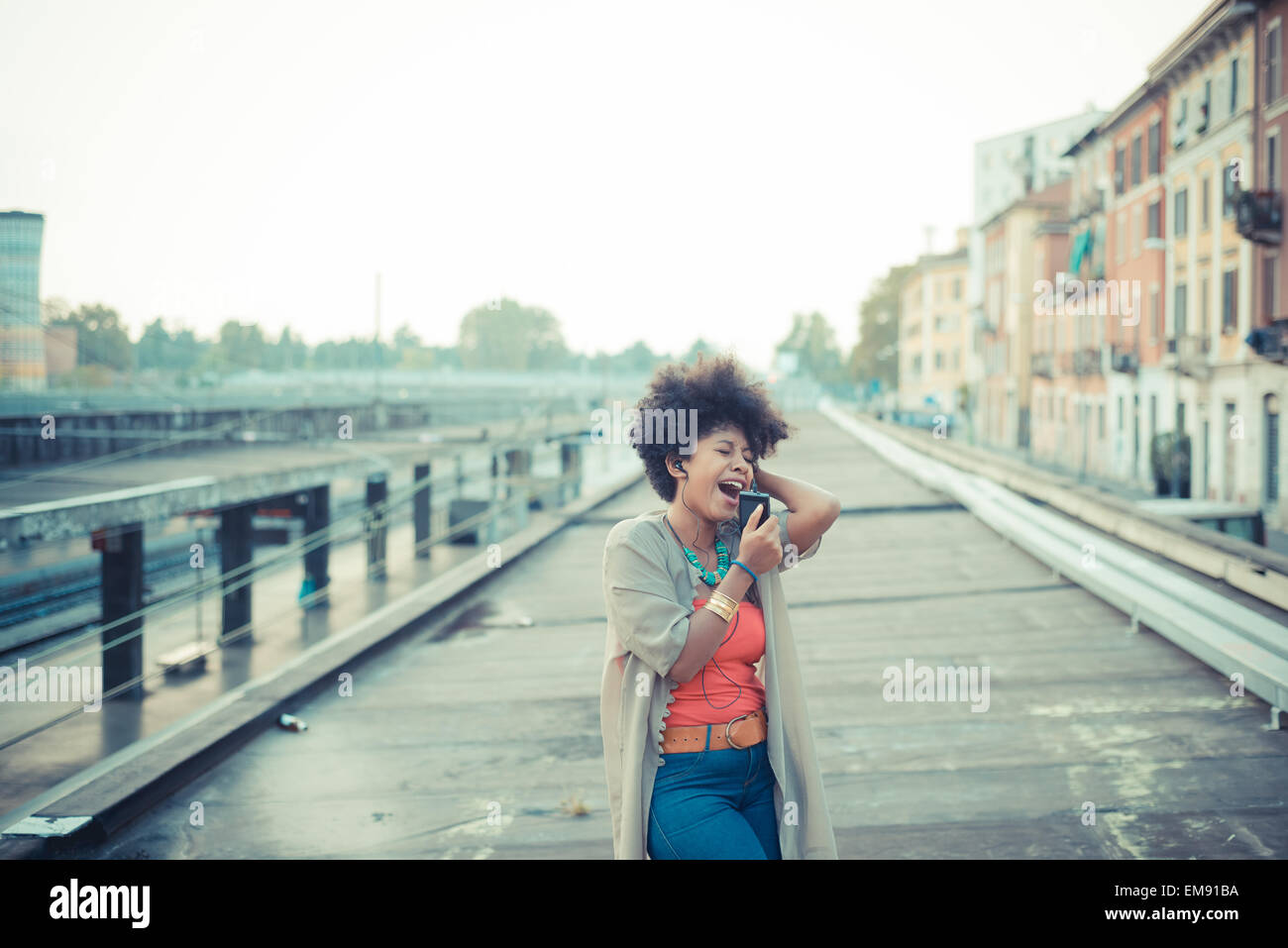 Junge Frau, die Musik von Smartphone im Industriegebiet der Stadt singen Stockfoto