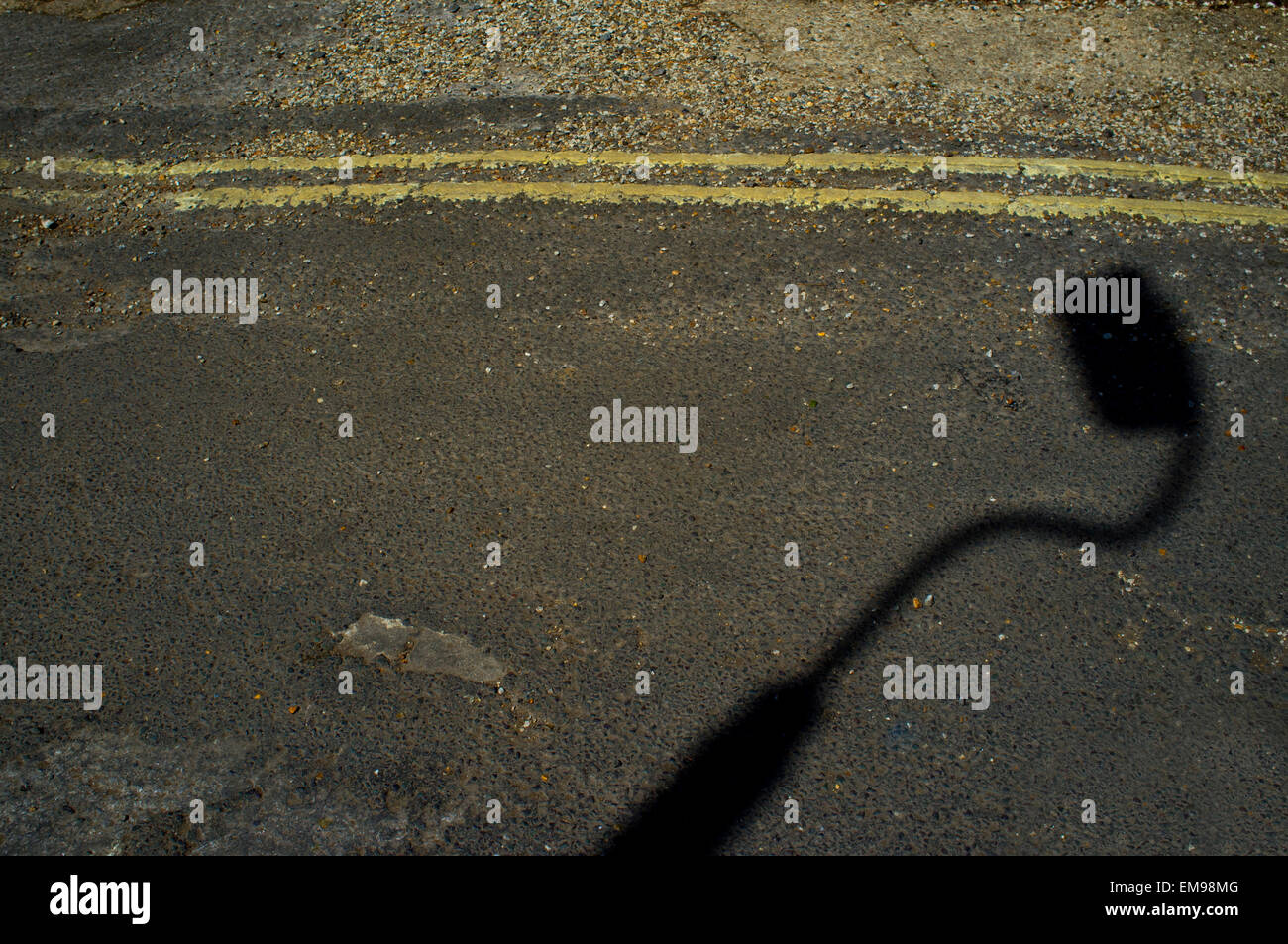 Schatten der Laternenpfahl auf Asphaltstraße mit gelben Doppellinien. Stockfoto
