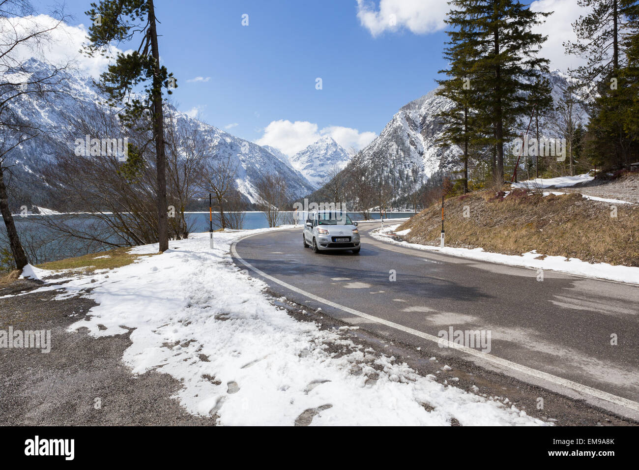 Ein Auto fährt rund um den See von Plansee, darüber, dass die schneebedeckten Alpen Stockfoto