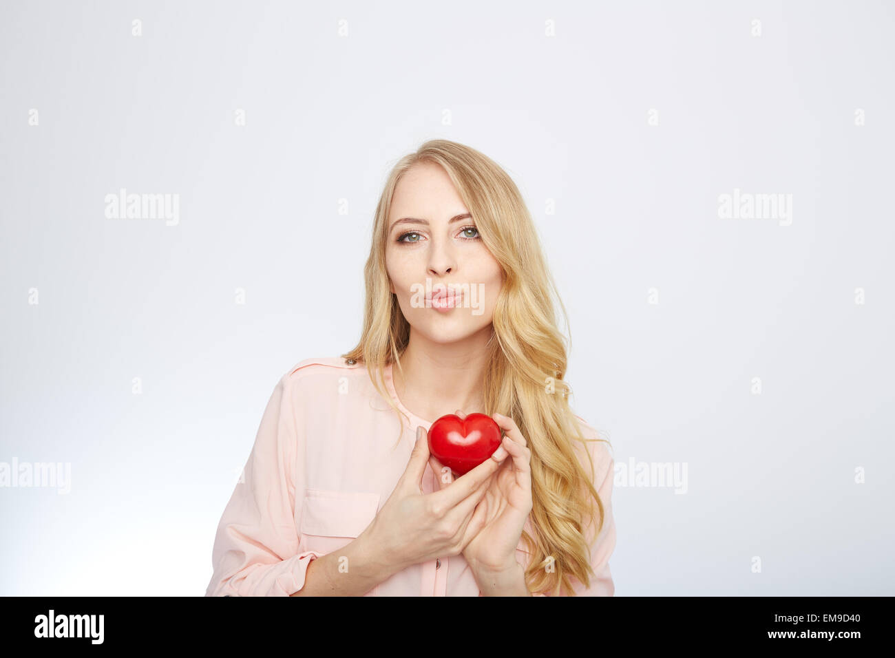 Junge, blonde Frau hält ein rotes Herz. isoliert auf weiss. Stockfoto