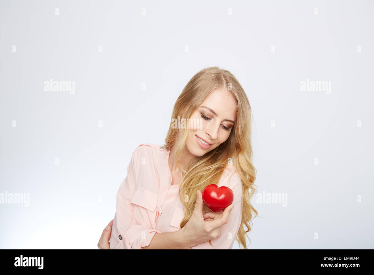 Junge, blonde Frau hält ein rotes Herz. isoliert auf weiss. Stockfoto