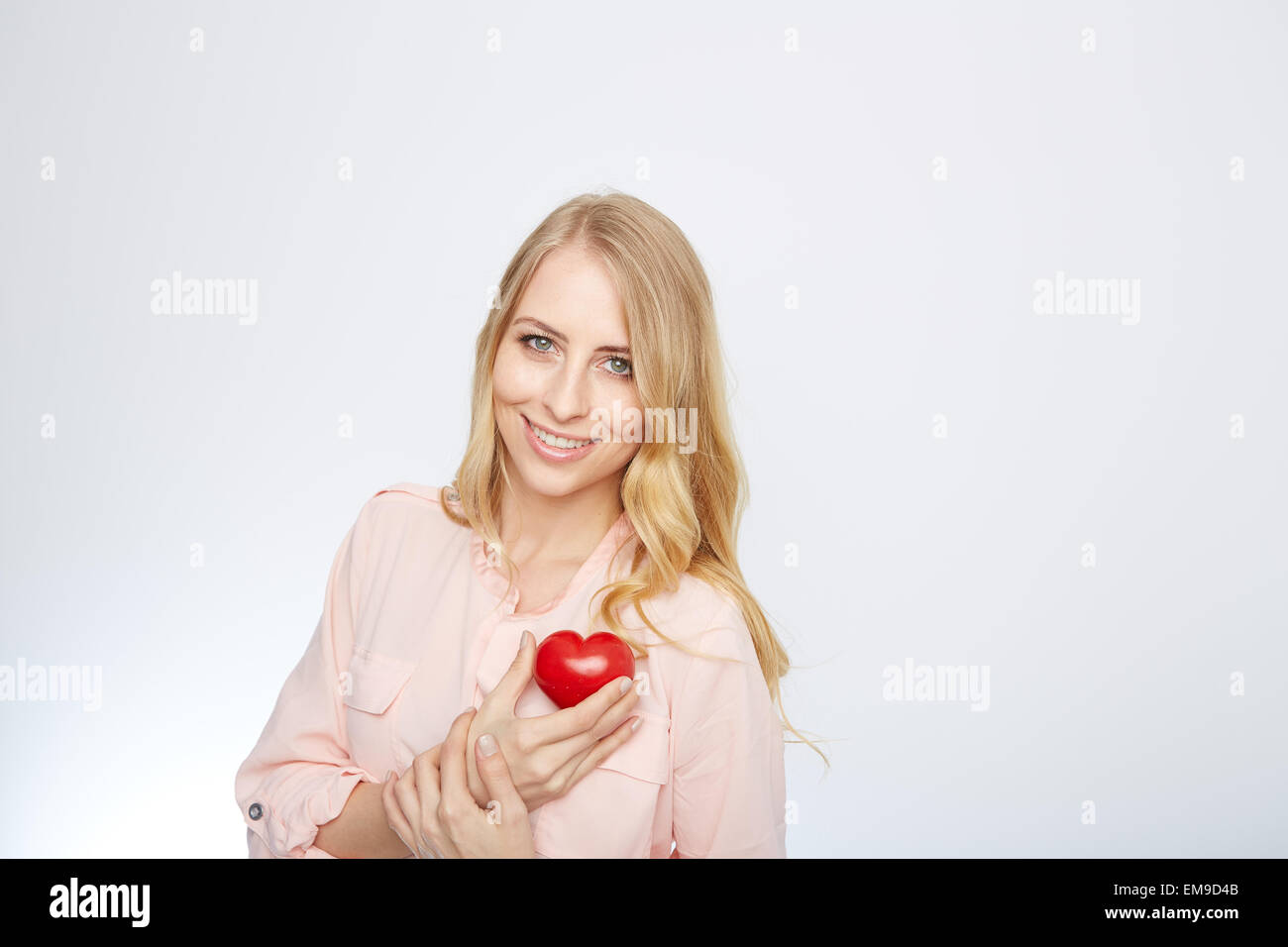 Junge, blonde Frau hält ein rotes Herz. isoliert auf weiss. Stockfoto