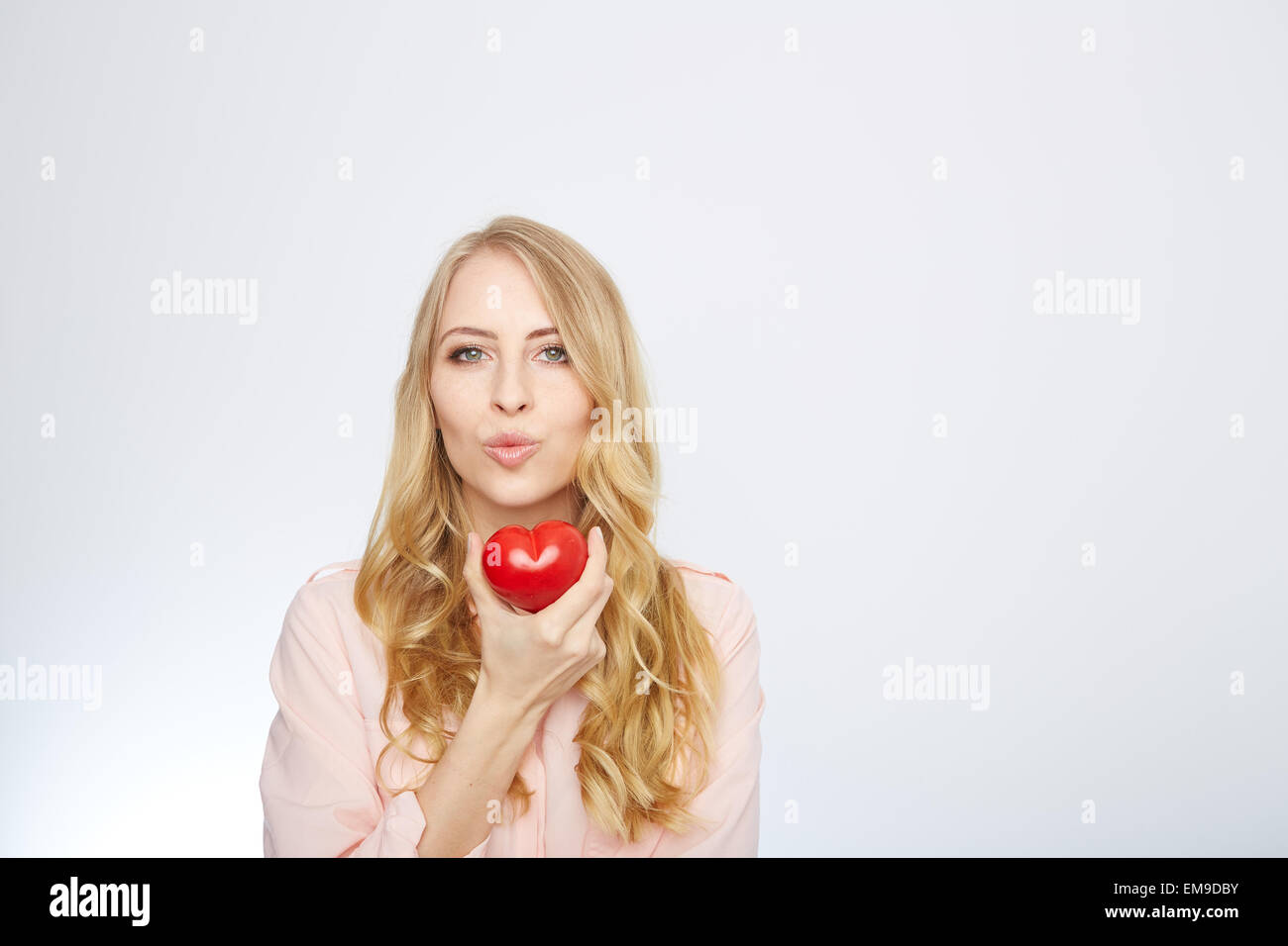 Junge, blonde Frau hält ein rotes Herz. isoliert auf weiss. Stockfoto