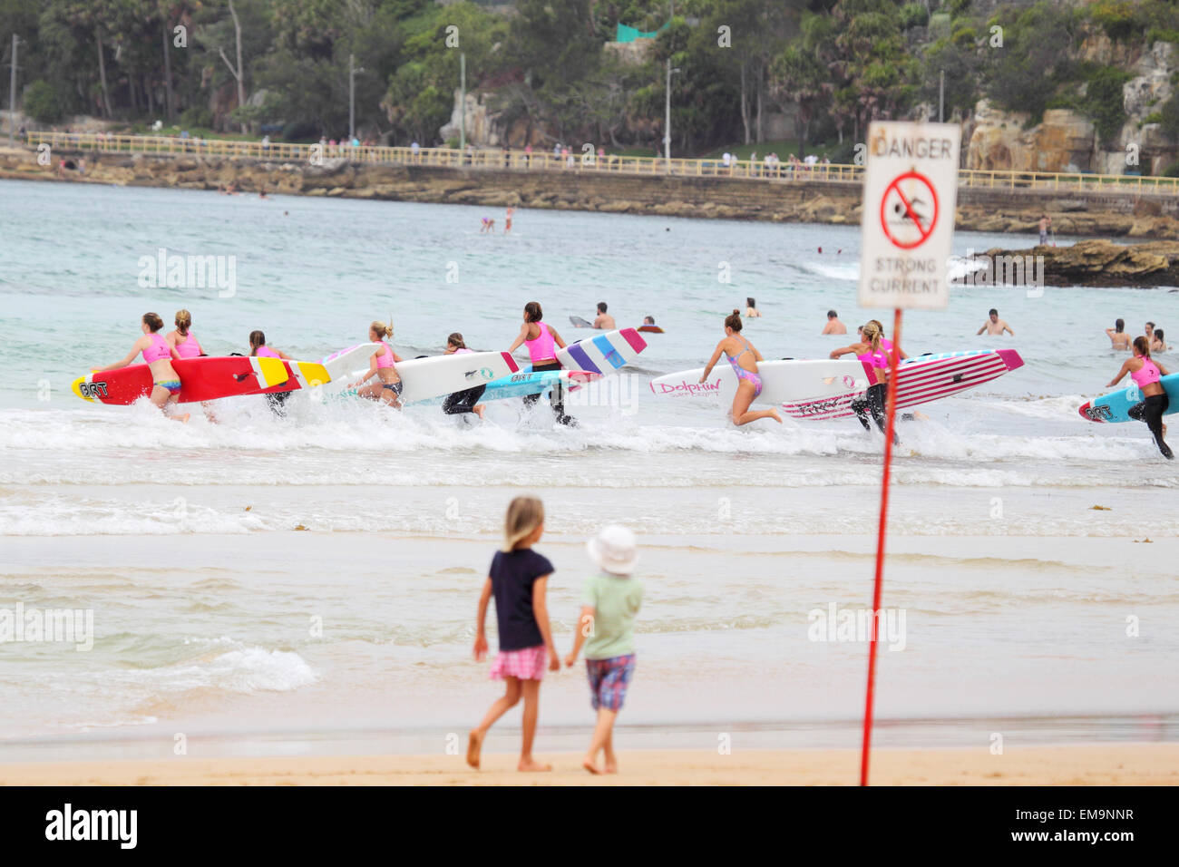 Schülerinnen und Schüler einer Surf-Schule läuft in die Wellen mit ihren Surfbrettern am Strand von Manly, Sydney, Australien. Stockfoto