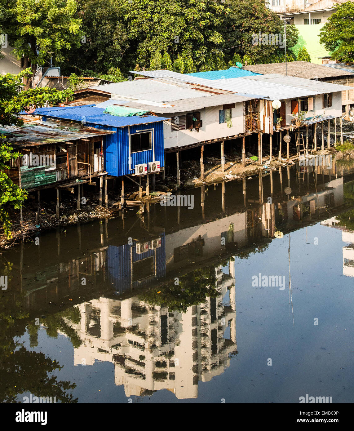 Riverside Slums in Bangkok mit der Reflexion des nahe gelegenen modernen Apartments, die über sie Webstuhl. Stockfoto