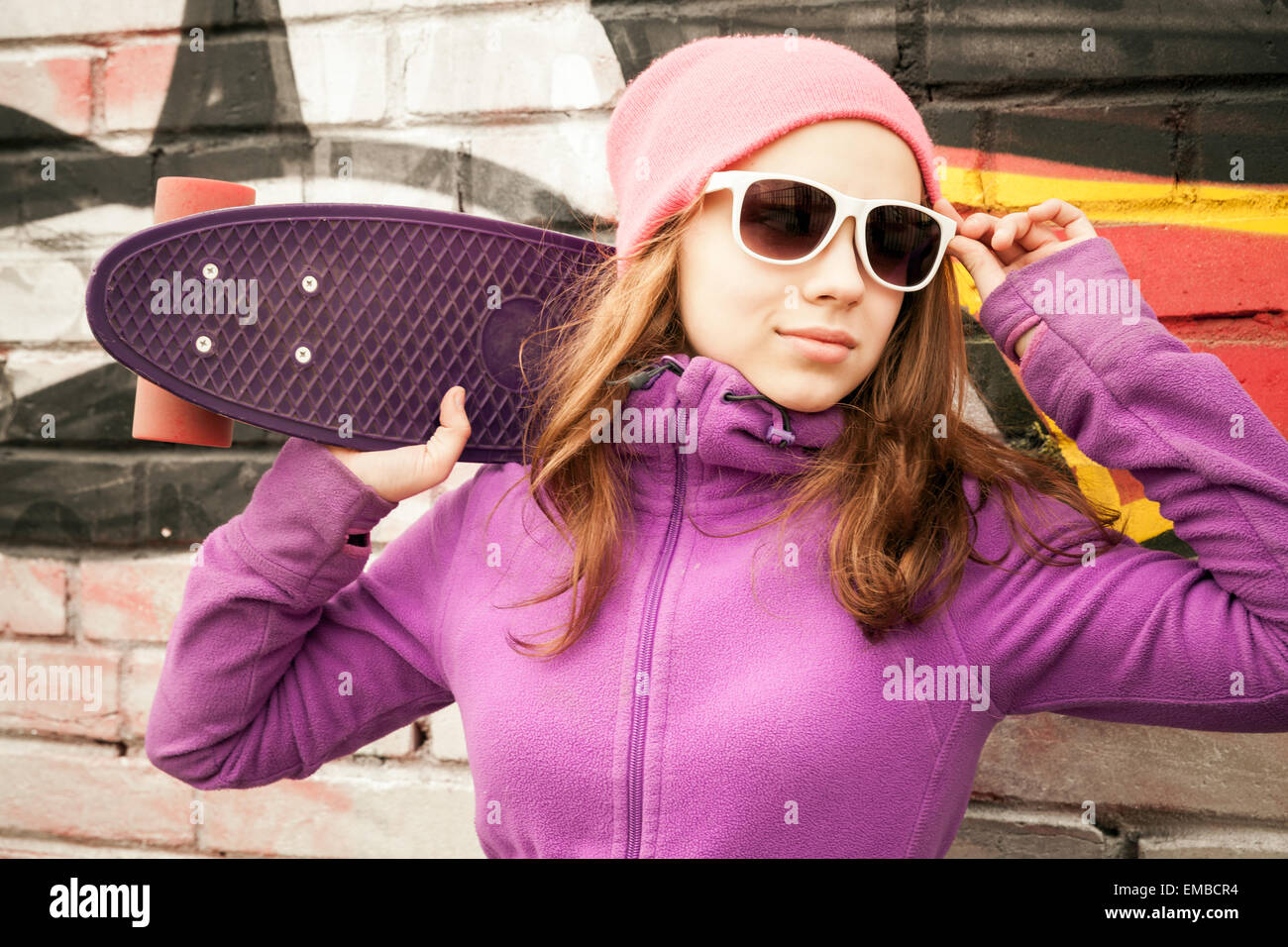 Blonde Teenager-Mädchen steht in der Nähe von urban Mauer mit Graffiti und hält eine skateboard Stockfoto