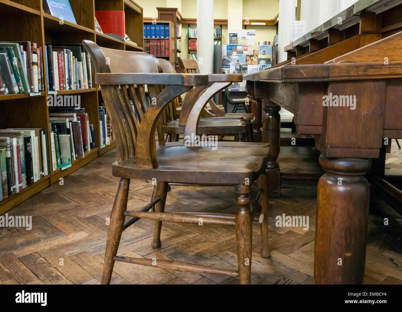 Holzstühle auf hölzerne Schreibtische mit Bücherregalen dahinter in Bristol Zentralbibliothek. Stockfoto
