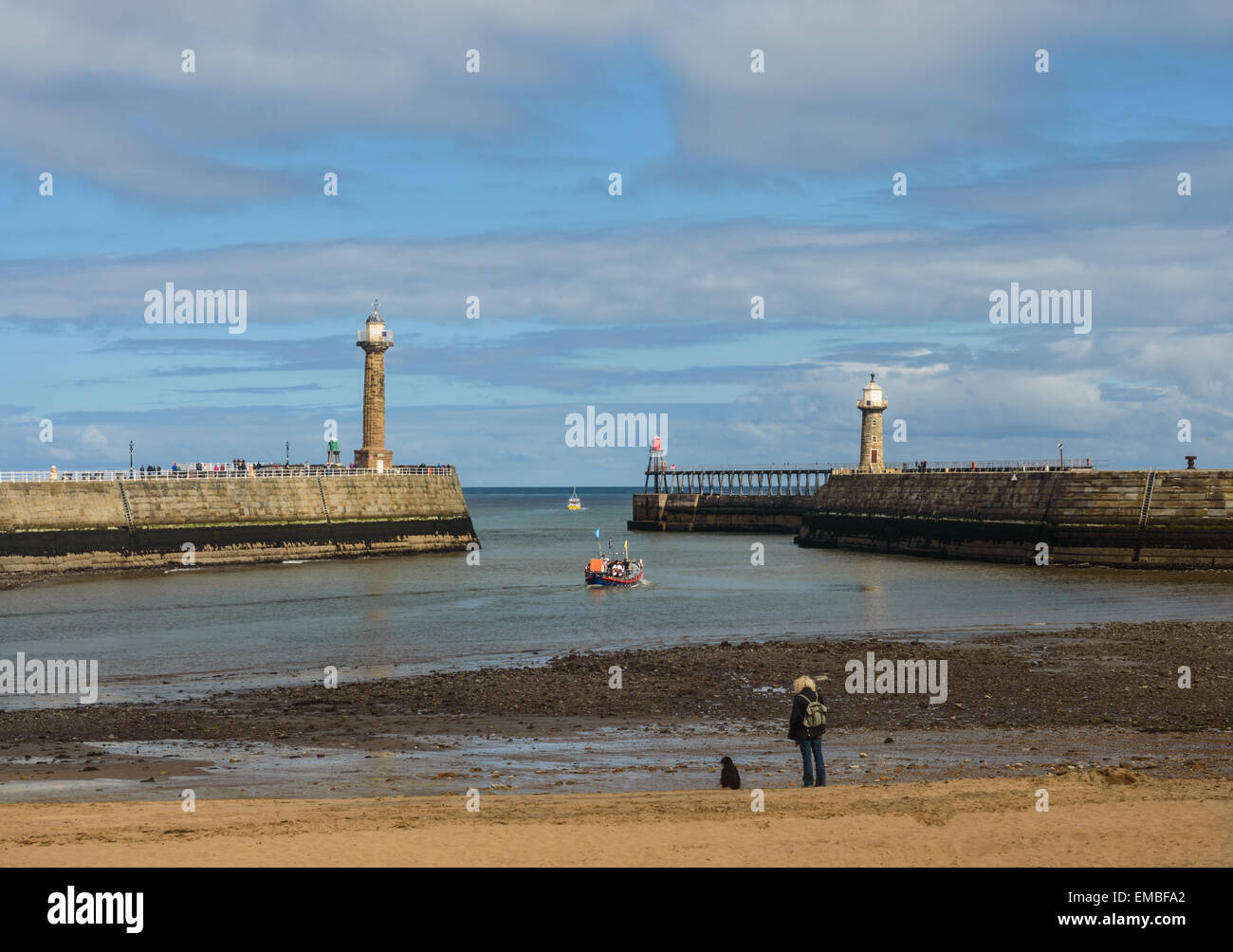 Es steht eine Frau mit ihrem Hund am Strand im Hafen von Whitby, North Yorkshire, England. Am 18. April 2015. Stockfoto