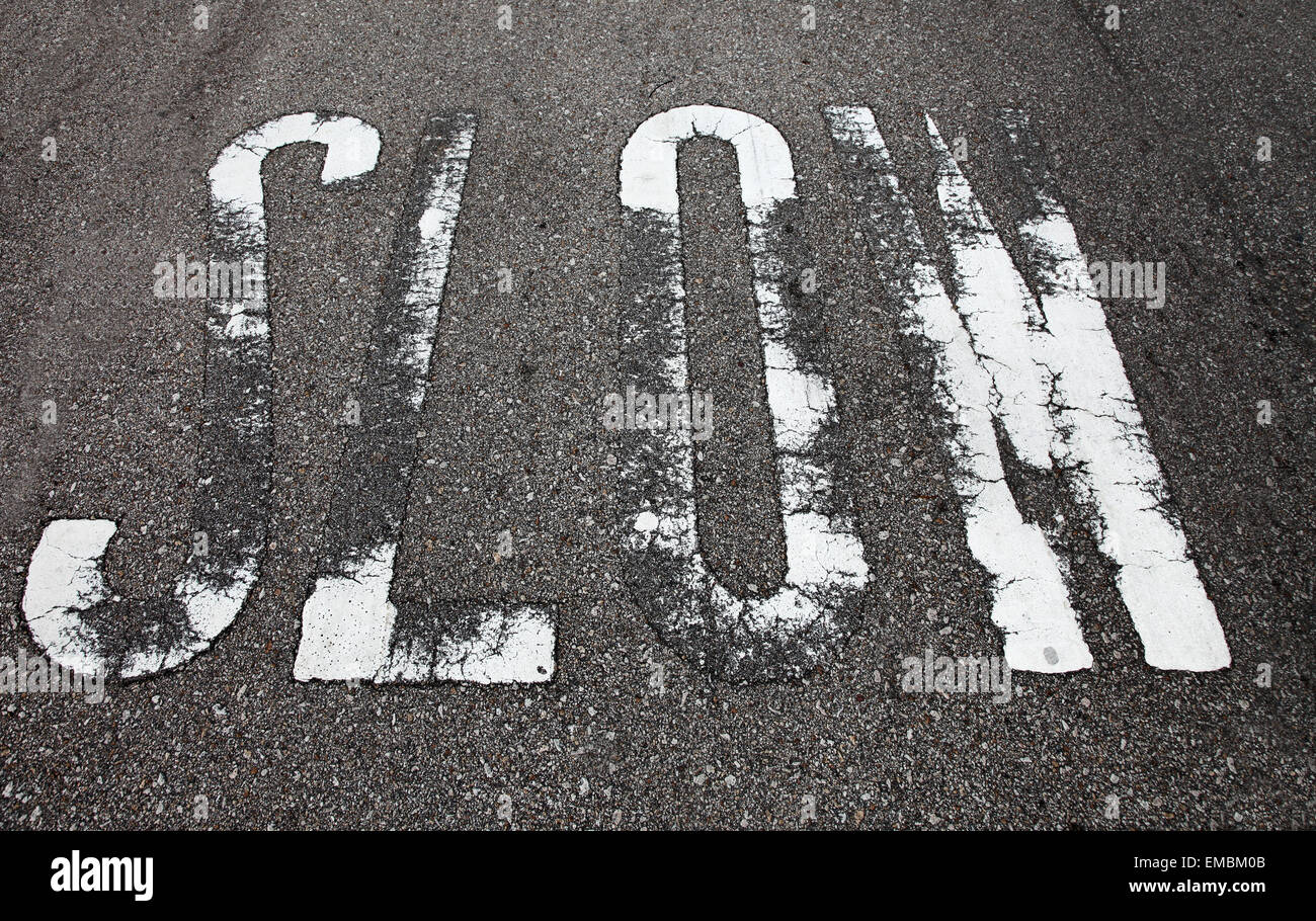 Es ist ein Foto von einem Straßenschild auf den Boden, der "SLOW", sagt gemalt Stockfoto