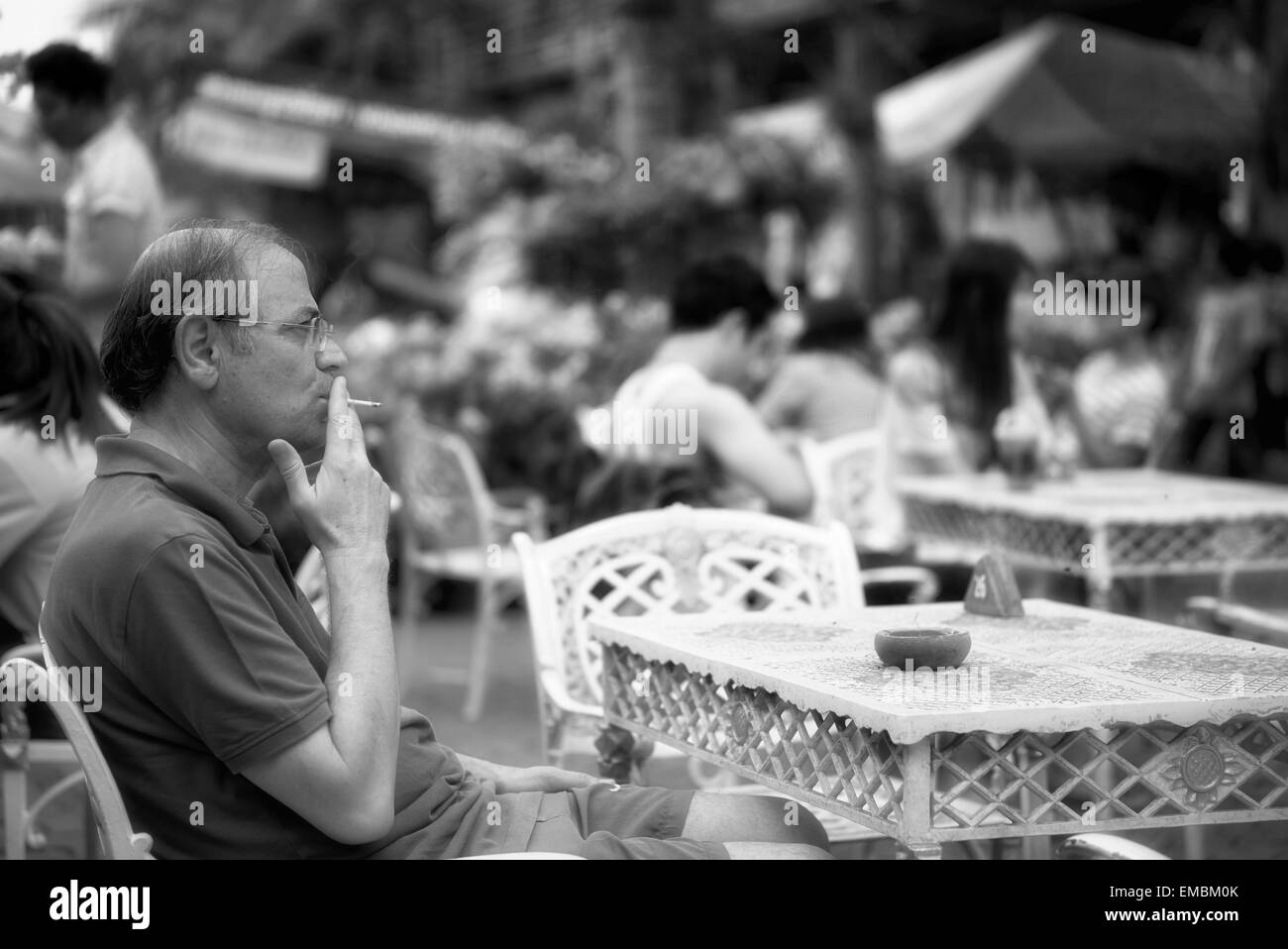 Mann raucht eine Zigarette und sitzt allein an einem Straßencafé Tisch. Schwarzweißfotografie Stockfoto