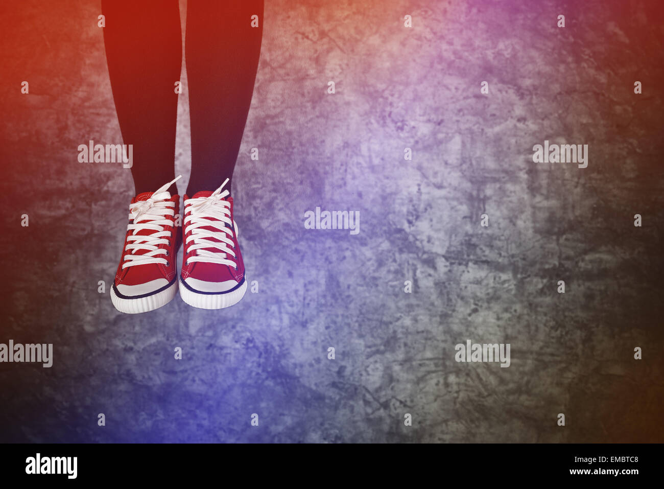 Unvorsichtige junge Teenager Frau springen vor Freude, rote Sneakers auf Grunge Hintergrund Stockfoto
