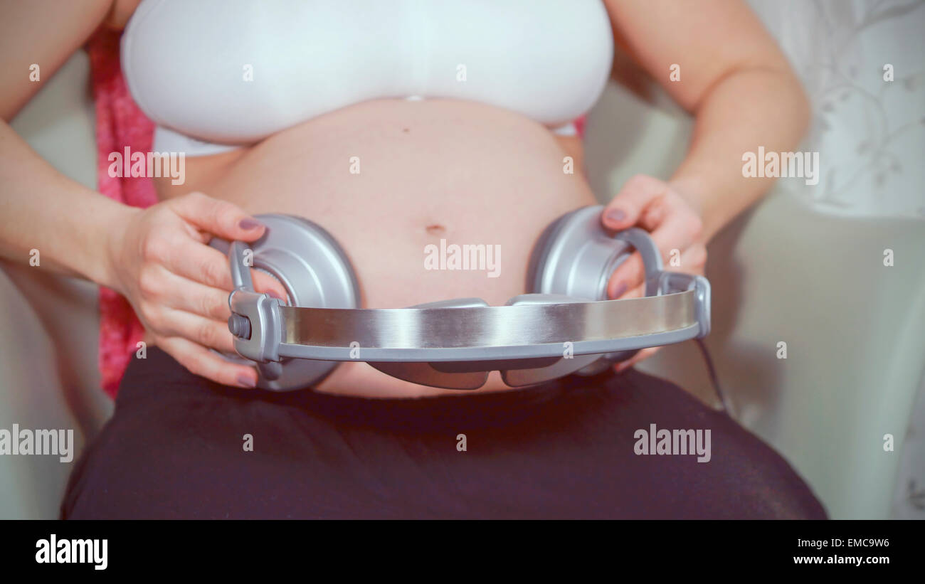 Schwangere Frau mit Kopfhörer zu Bauch Stockfoto